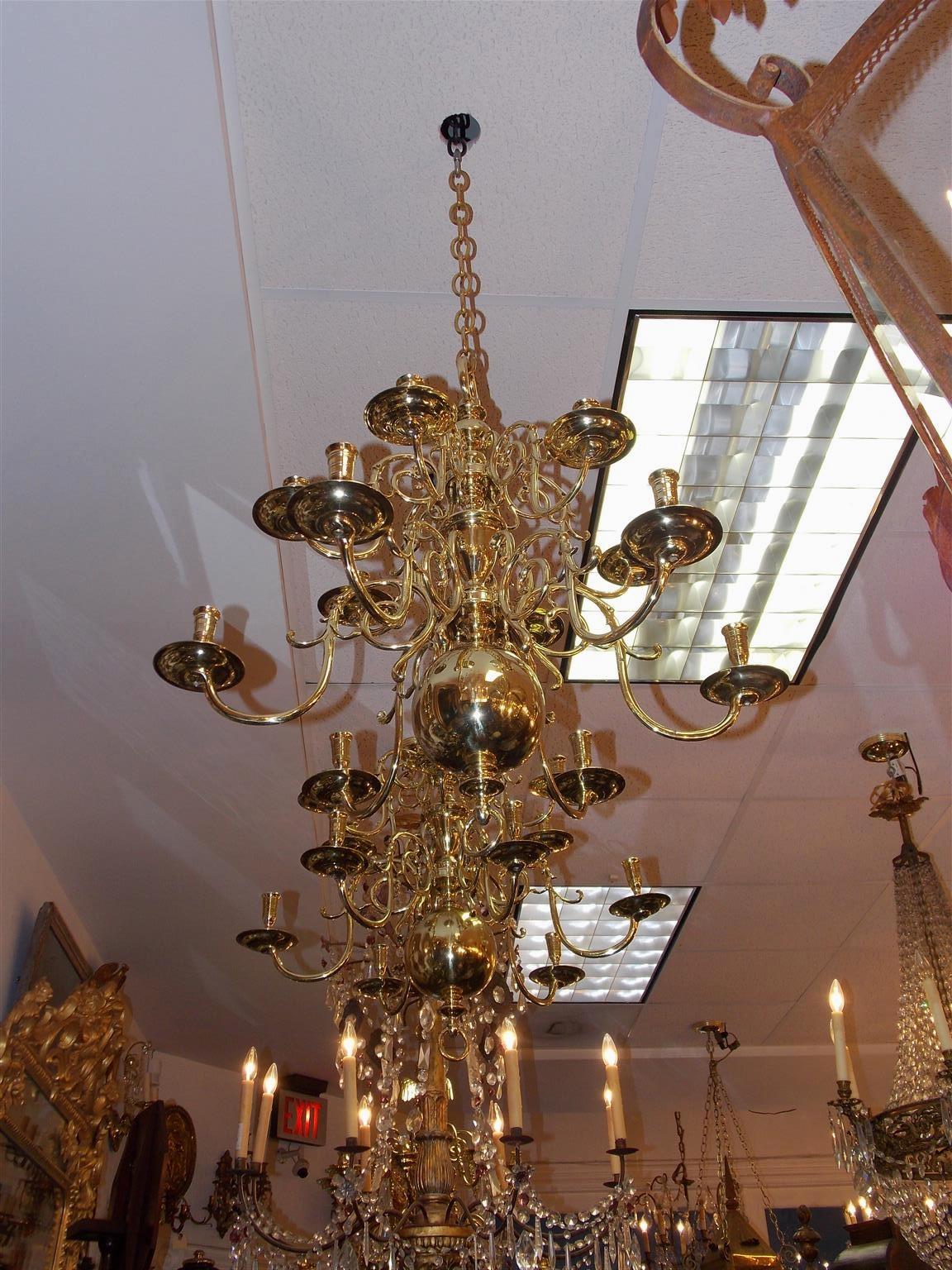 Pair of Dutch colonial brass two-tiered twelve light chandeliers with scrolled decorative arms, original bobeches, centered bulbous column, and terminating on a large ball with centered ring finial. Chandeliers are candle powered and can be