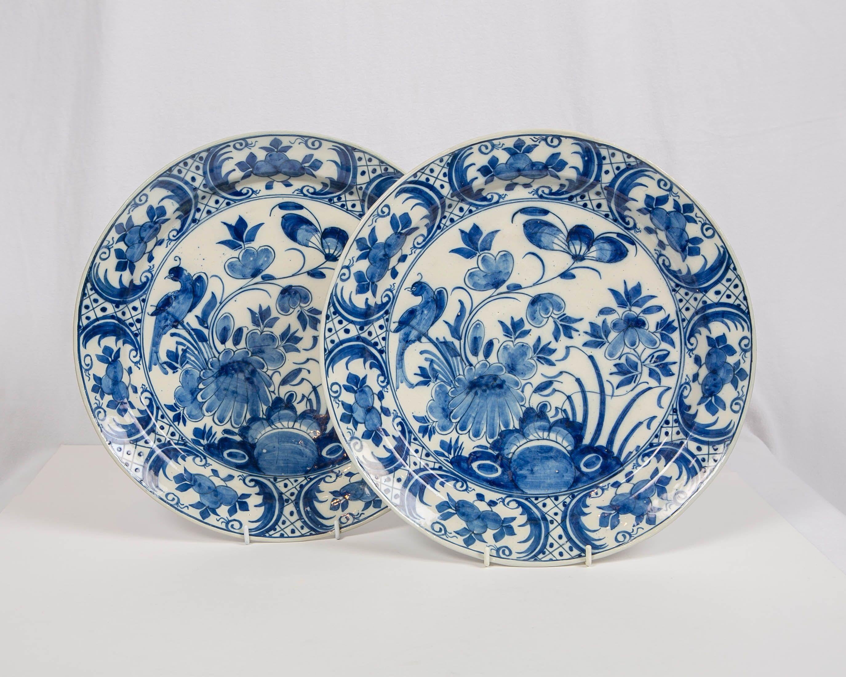 A pair of 18th century Dutch Delft blue and white hand-painted chargers each showing a songbird resting on a flowering branch. The garden is lush with flowers. The artist has captured the essence of a garden so beautifully that you feel that it