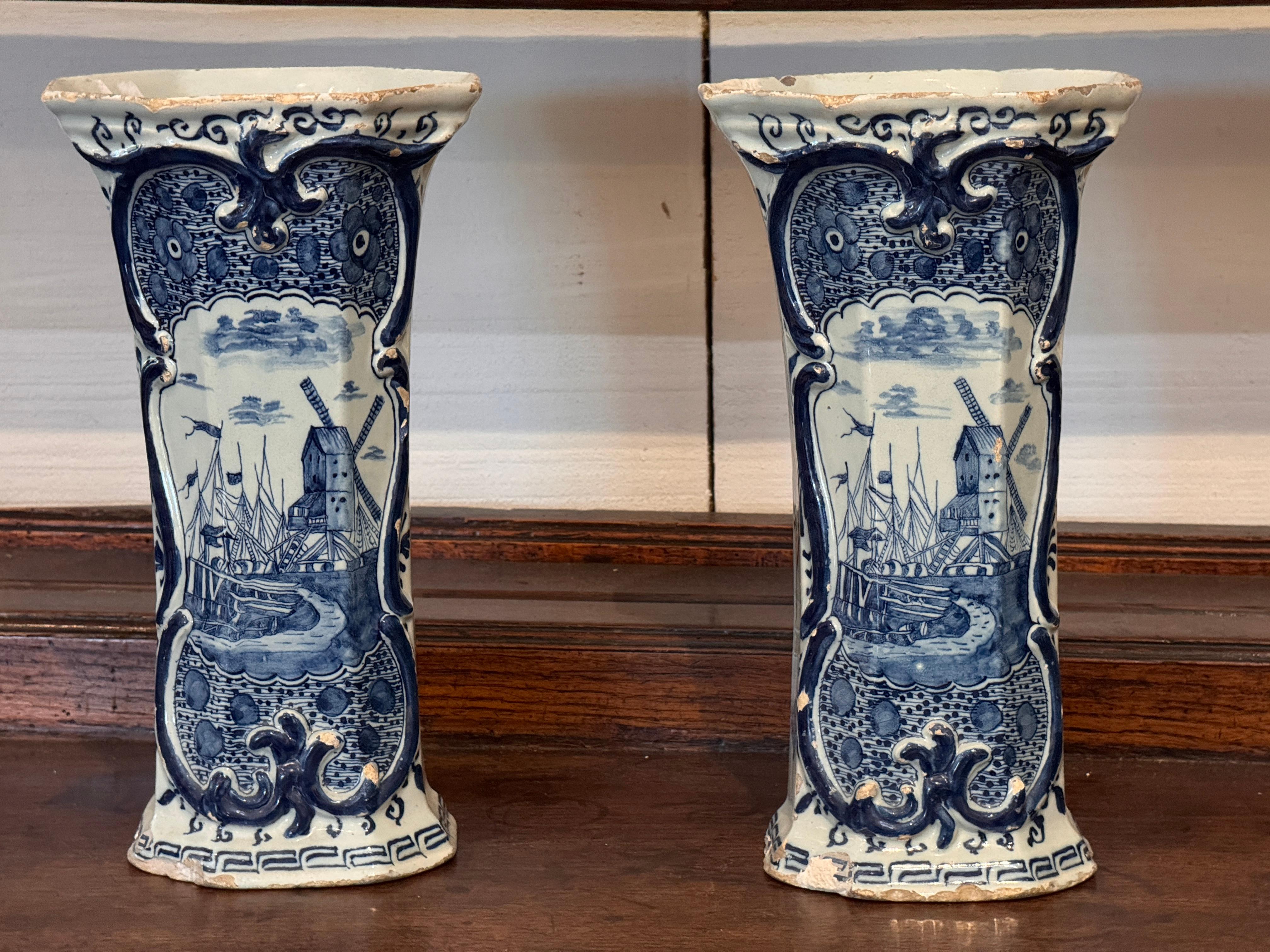 Paire de vases de Delft décorés en bleu et blanc de moulins à vent peints, de bateaux et de scènes de paysage dans des cartouches façonnés. Les bords évasés et les bordures à volutes ajoutent à leur attrait décoratif. L'usure et l'effritement de la