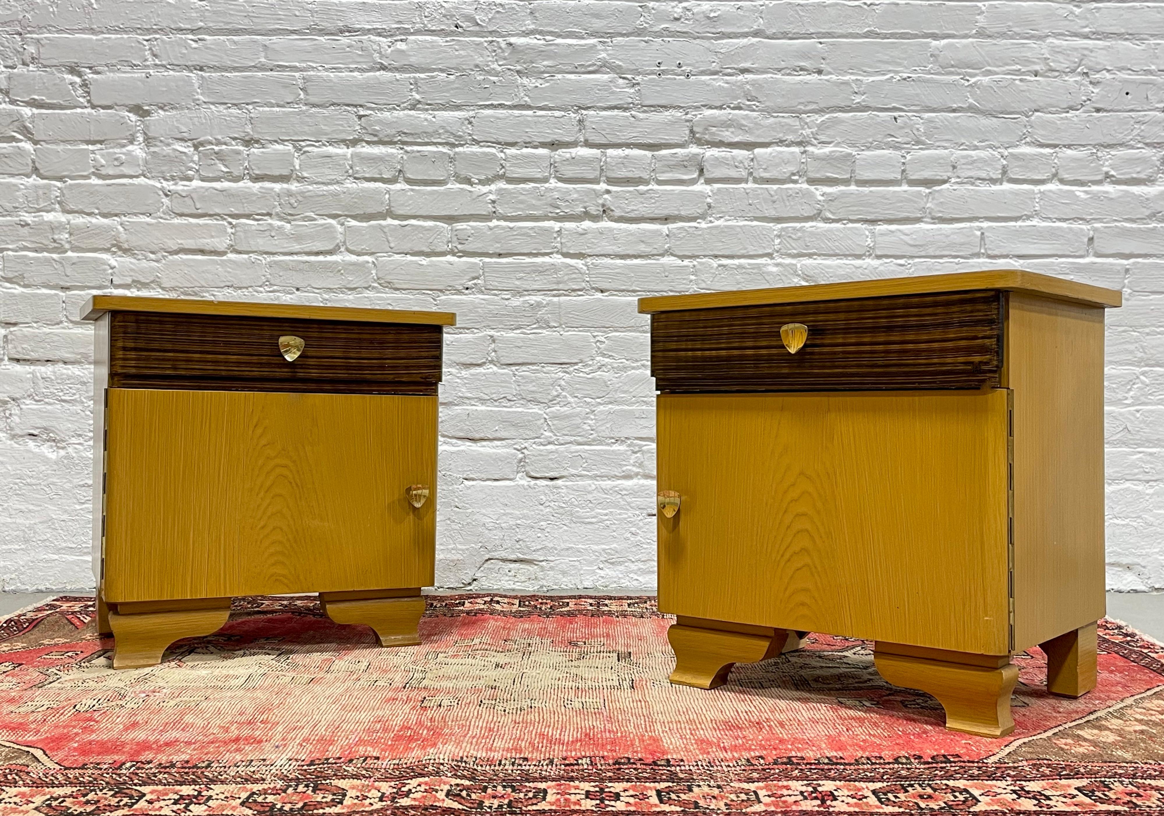 Pair of Dutch Modern Nightstands, c. 1950's. This lovely pair has an art deco flair with gorgeous legs and gold colored pulls. Gorgeous two tone design - easy to match with other wood tones. Each nightstand has a drawer and open space behind the