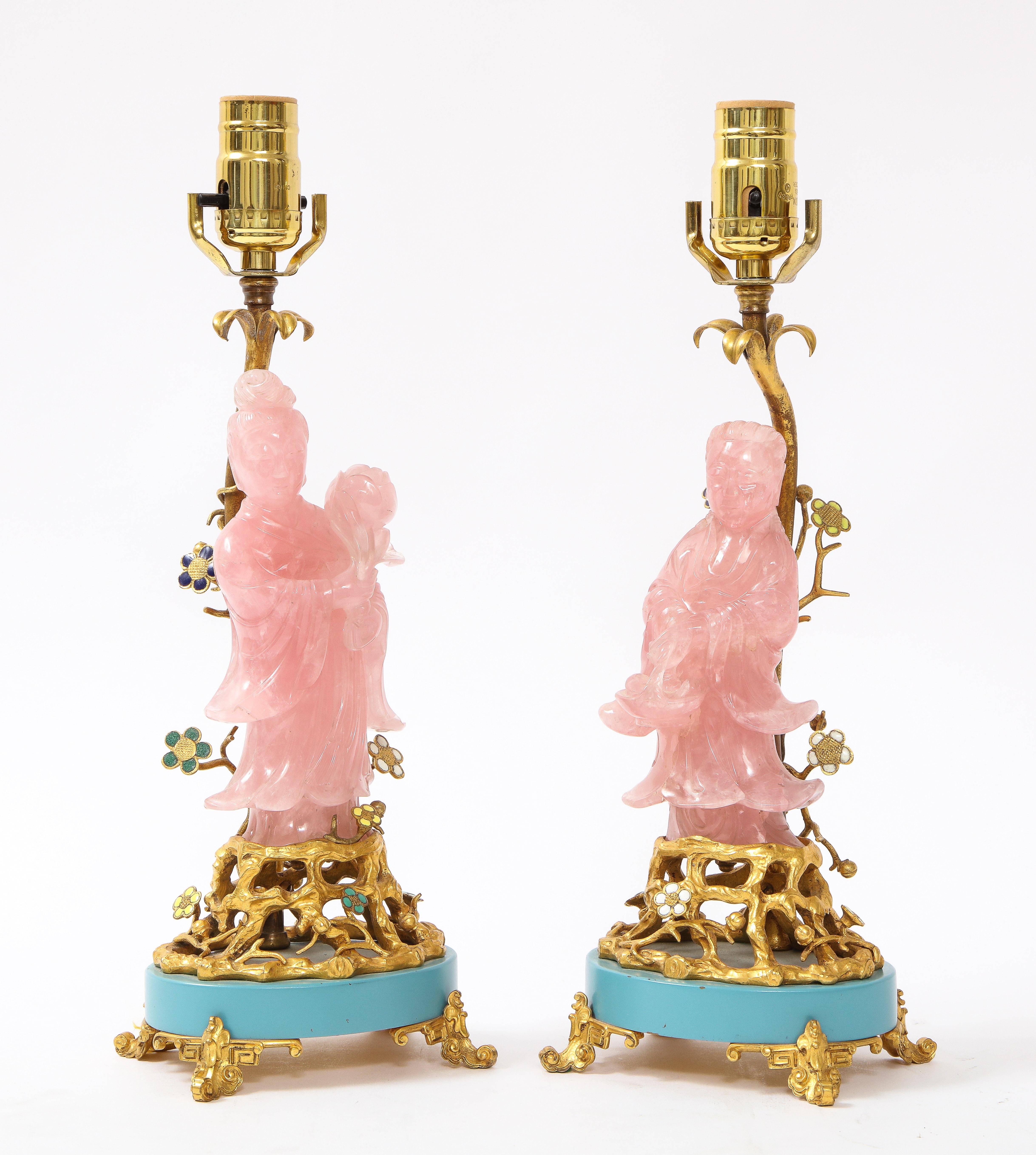 A fantastic pair of marked E. F. Caldwell and Co. Louis XVI style dore bronze mounted hand-carved rose quartz and enamel table lamps. Mounted on two dore bronze open work bases with blue enamel decoration and dore bronze Asian inspired feet are two