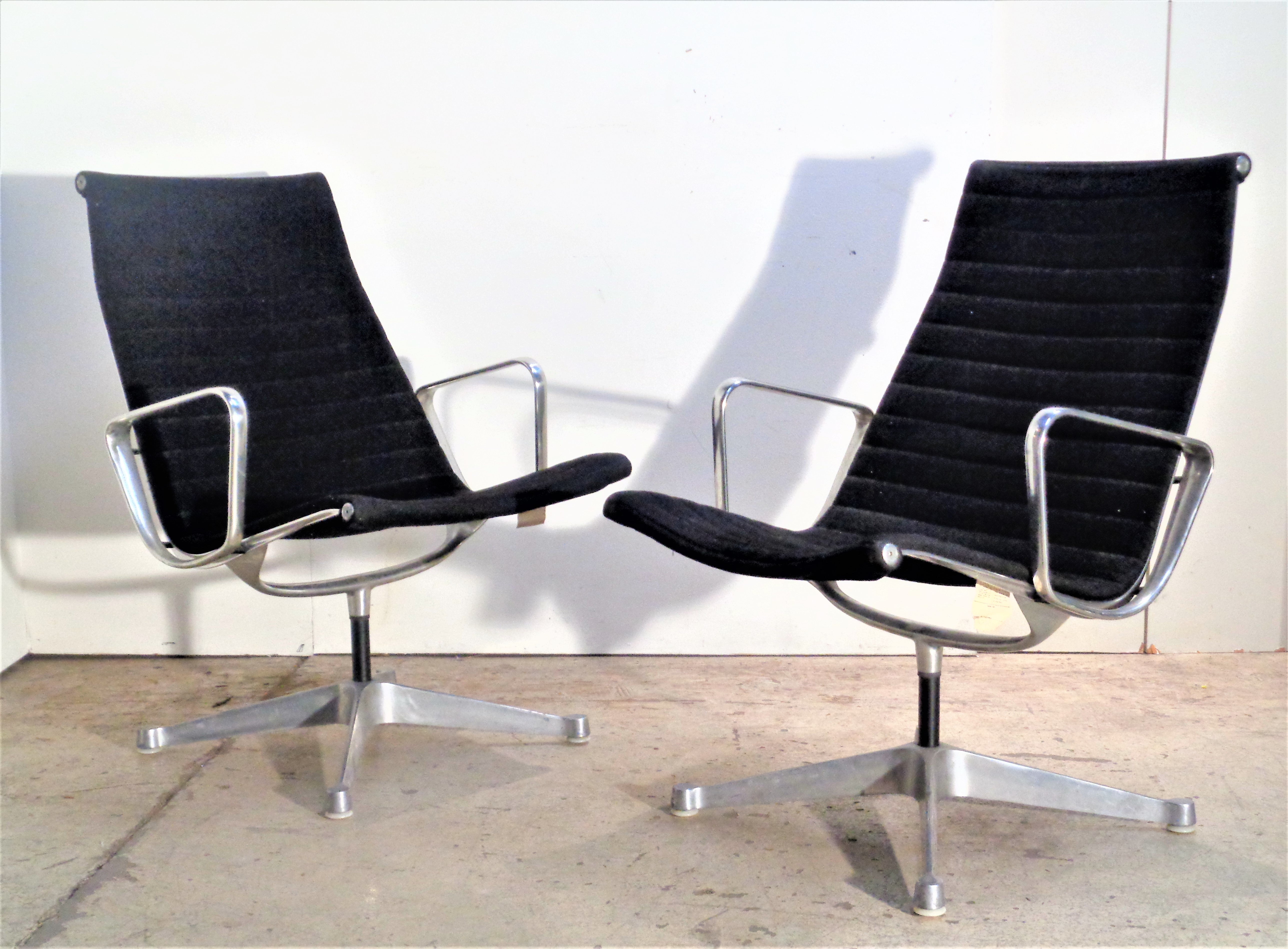 Pair of aluminum group armchairs designed by Charles and Ray Eames for Herman Miller in all original vintage condition w/ four star swivel base, nylon foot pads, black wool upholstery. Stamped signed into underside aluminum metal and with tag (