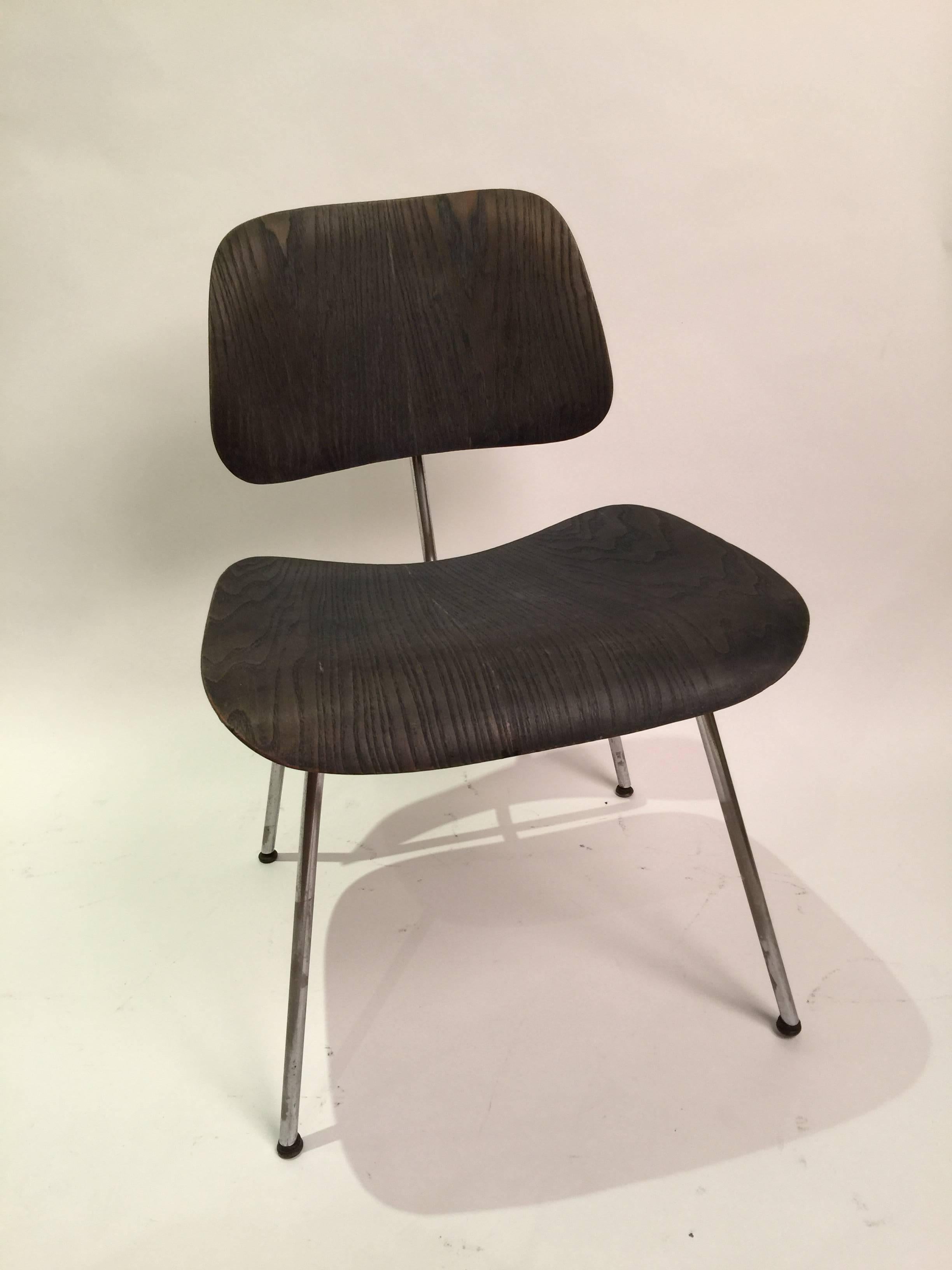 Pair of black aniline DCM dining chairs by Charles and Ray Eames. These first edition chairs were produced by Evans manufacturing and distributed by Herman Miller. Both chairs have labels intact. One chair shows some additional signs of use and has