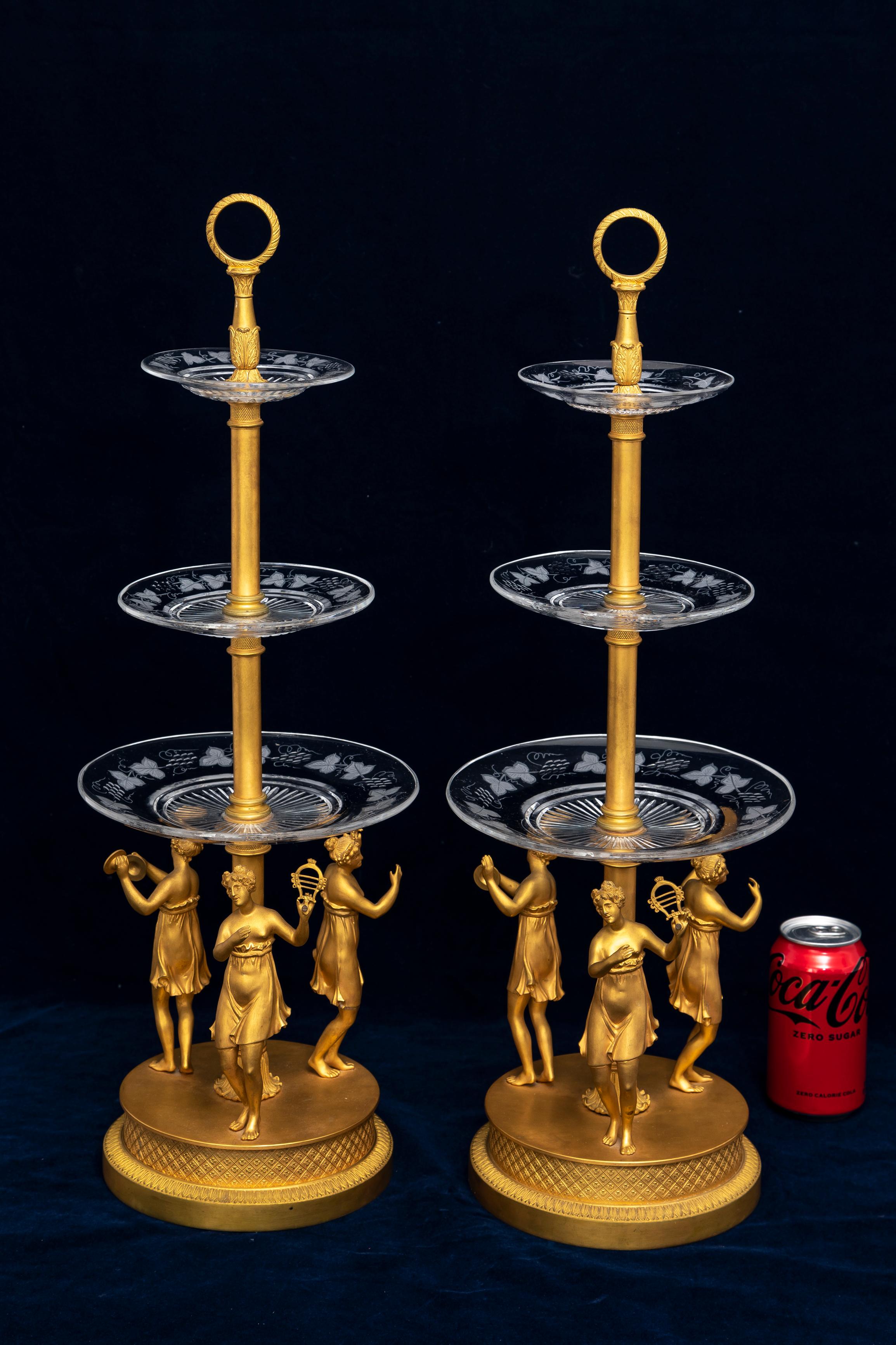 This pair of Empire-style tazza centerpieces showcases a sophisticated blend of finely cast bronze and Baccarat crystal in a striking three-tier structure. Each tazza is grounded by a solid bronze base, supporting tiers of Baccarat crystal bowls