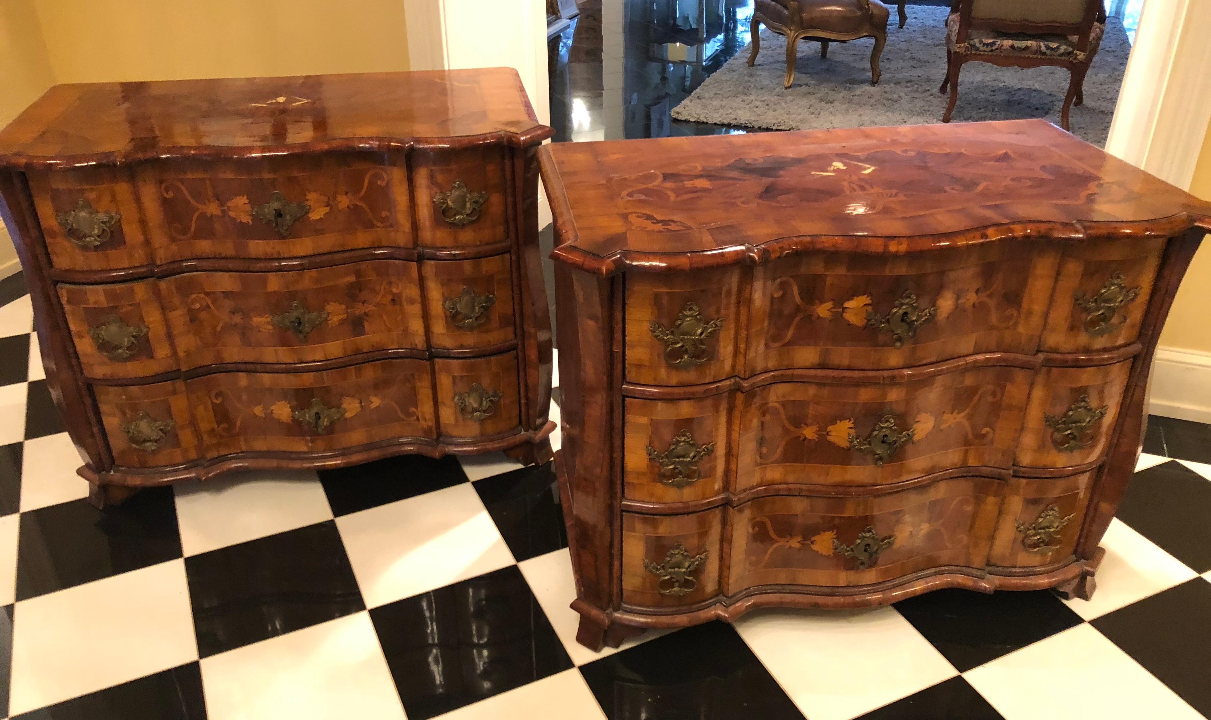 This extraordinary pair of early 18th century Bavarian commodes have exaggerated serpentine and Bombay shaped fronts with three drawers. Made of Circassian walnut with intricate inlaid floral and geometric marquetry in exotic woods the tops of each