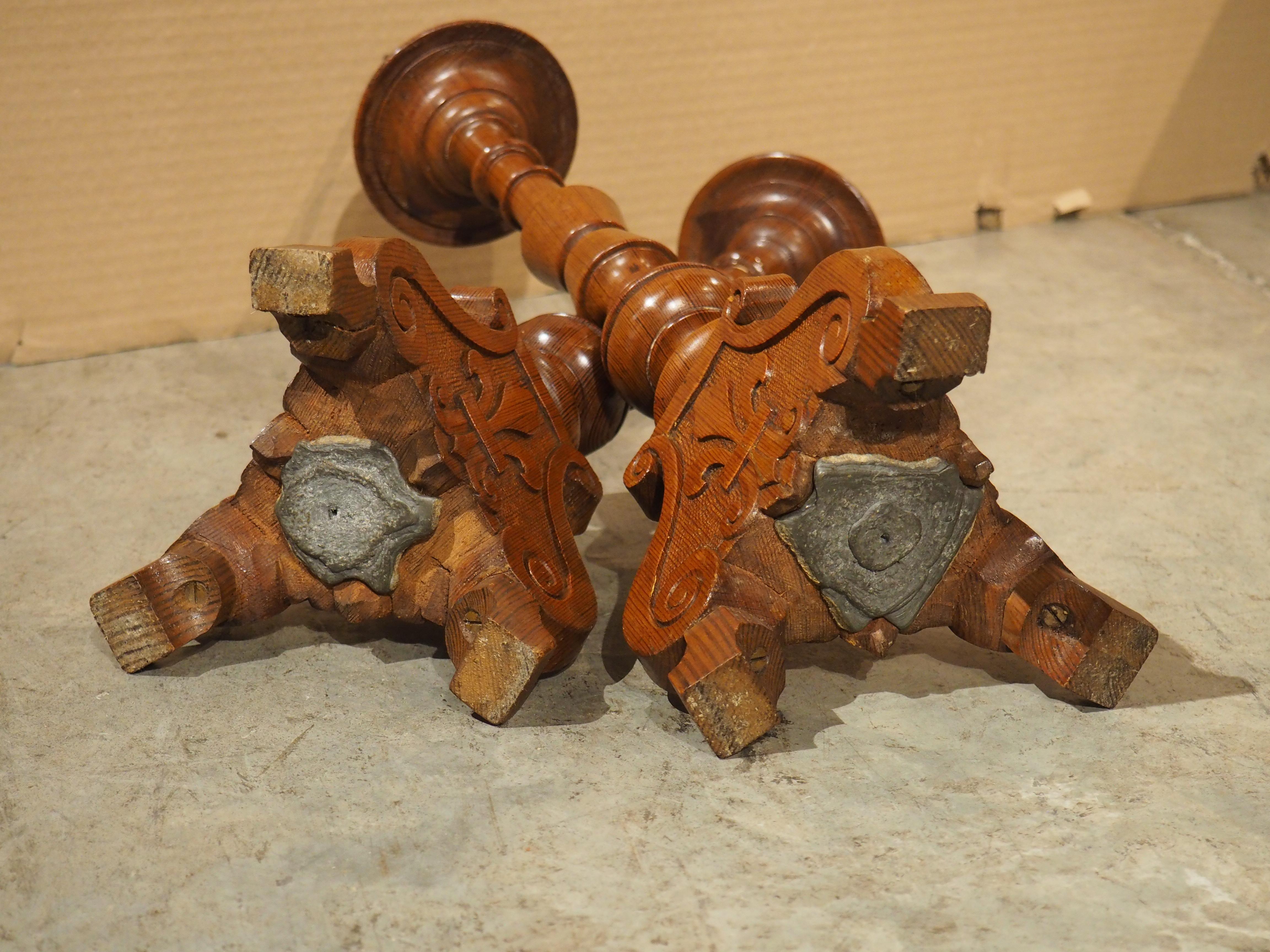 The pine wood of these French candlesticks has a beautiful satiny brown patina with darkened grains that truly stand out. Hand-carved in the early 1900s, the candlesticks have a tripartite base, with each side adorned with a low-relief carving of a