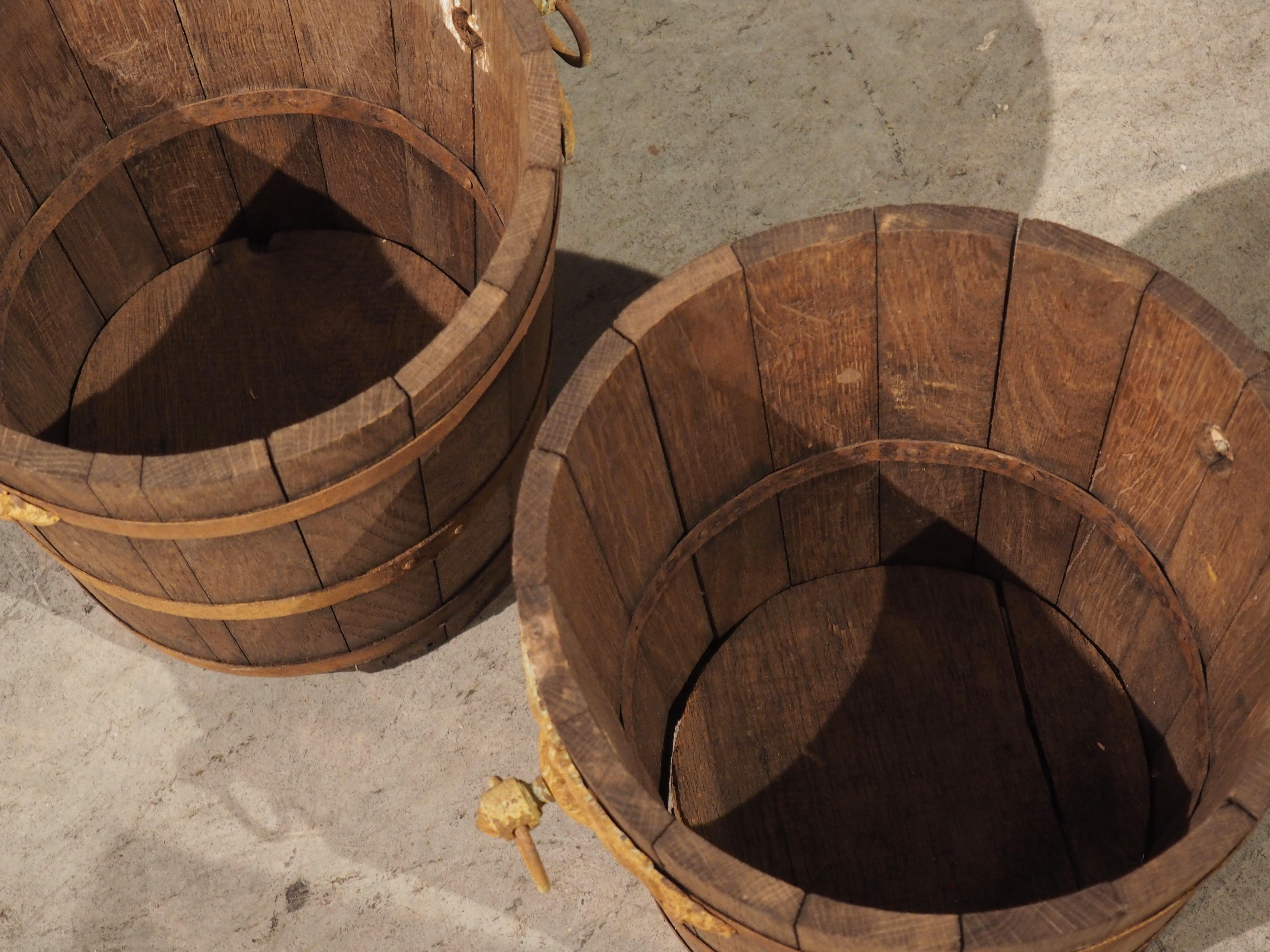 Enveloped with three circumferential bindings, this pair of French oak and iron buckets have held their form very well. hand carved from oak in the early 1900s, the wood has a deep brown color. Each bucket is also adorned by three straps, a pair of