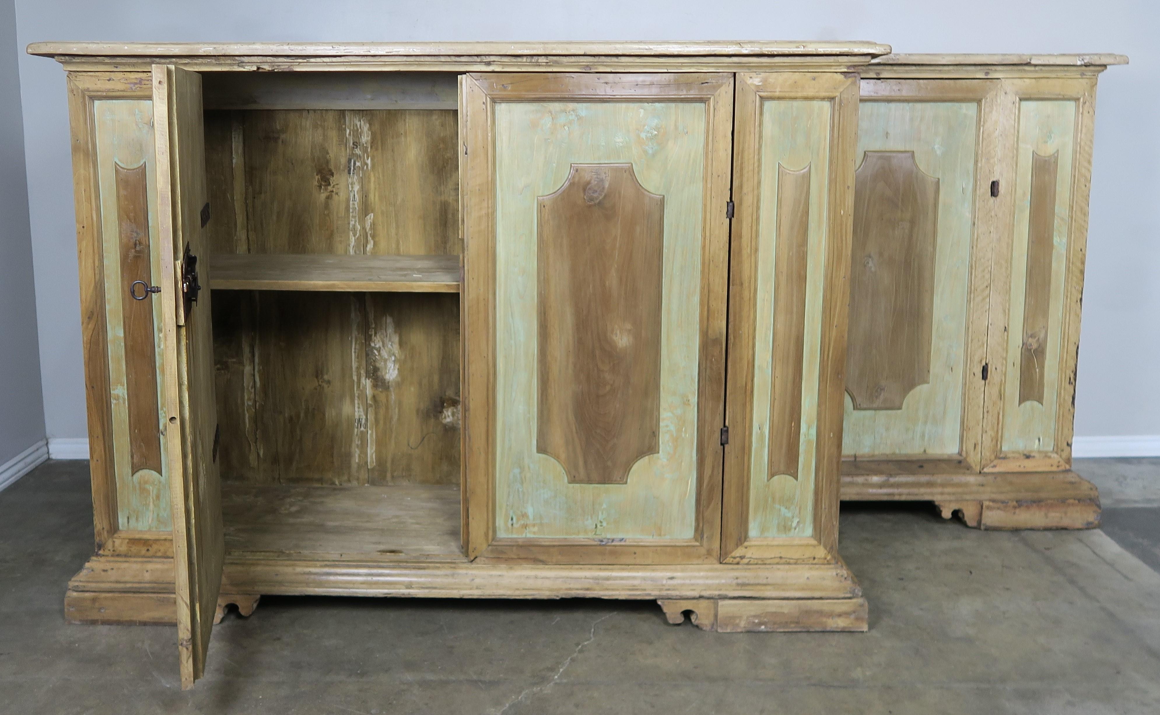 Pair of early 19th century Italian walnut painted sideboards with two doors and single shelf on each cabinet. The paint is beautifully worn to a soft celadon coloration. Original wrought iron hardware and locks.