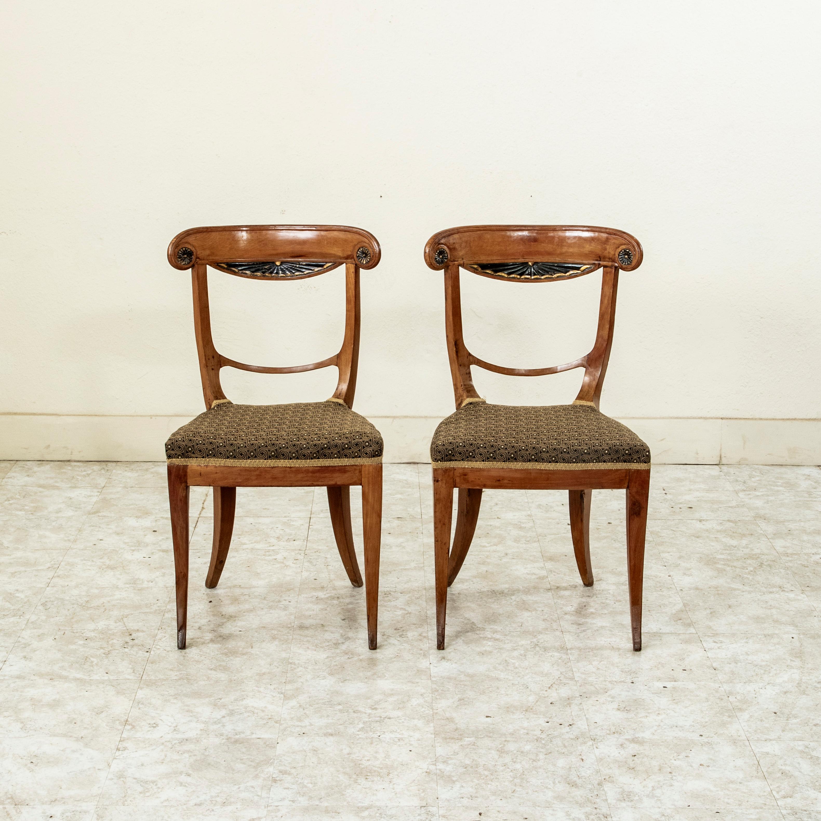 This pair of early nineteenth century Austrian Biedermeier period walnut and ebonized pearwood chairs features a curved seat back with scrolling sides finished with medallions. The center of the seat backs is finished with a carved drapery motif and