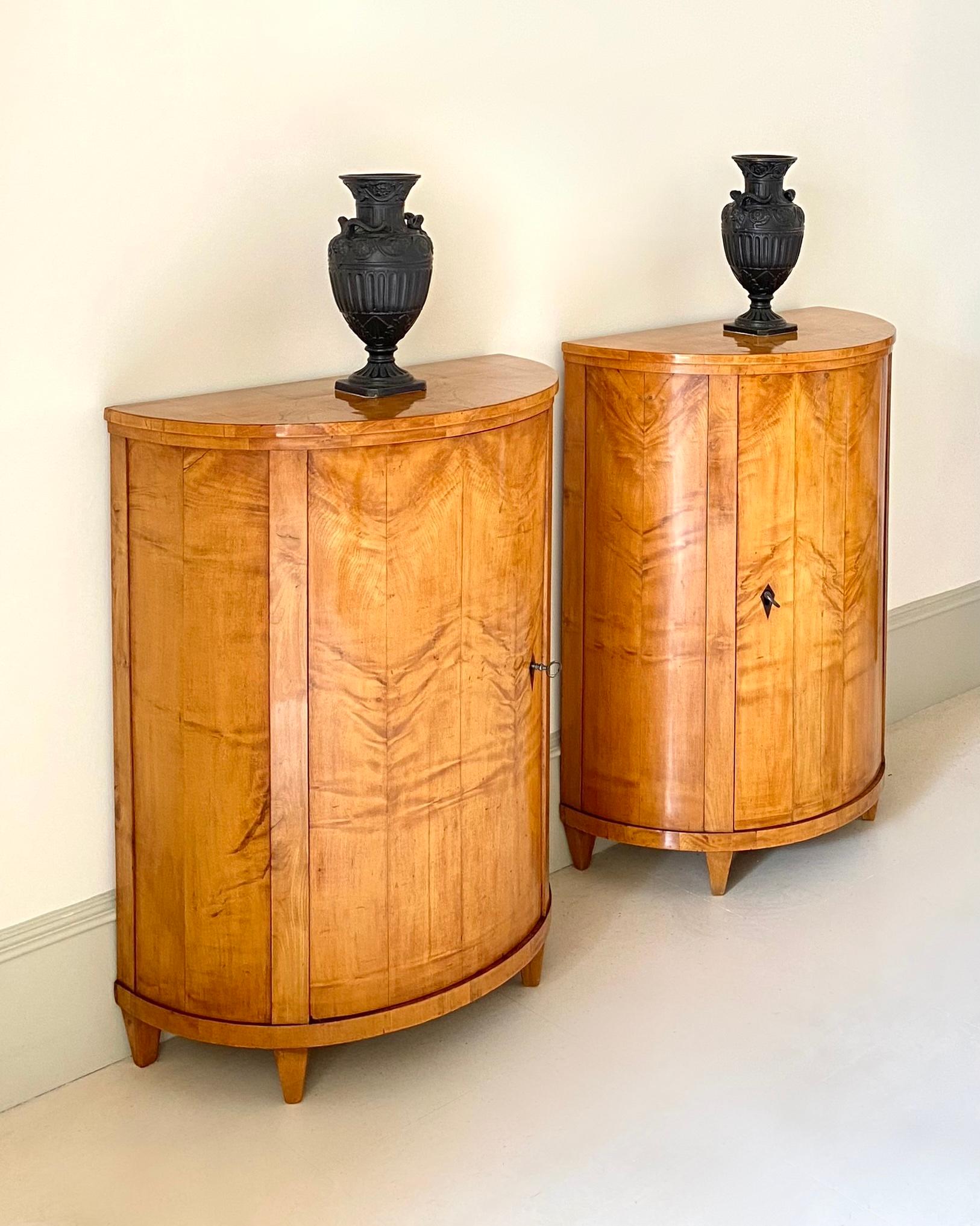 Beautiful, very rare pair of neoclassical Biedermeier demi-lune side cabinets, maple veneered and original ebony keyholes. 
A middle door with compartments inside.
North Germany, around 1820.