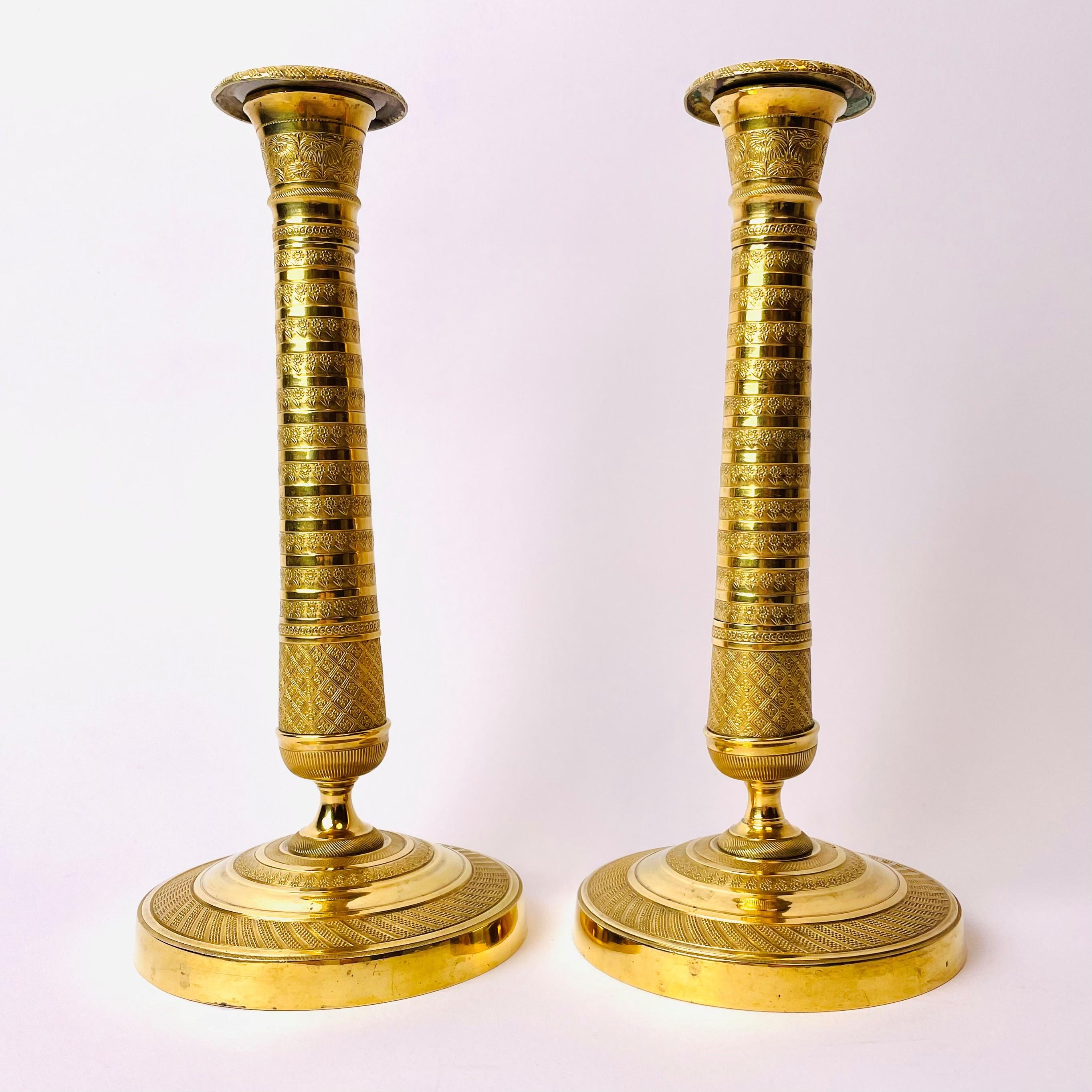 Excellent pair of early 19th century candlesticks in gilt bronze. These neoclassical Empire Candlesticks are made in France, circa 1820. Unusual model with stripes and beautifully stylized floral decorations.

Wear consistent with age and use.