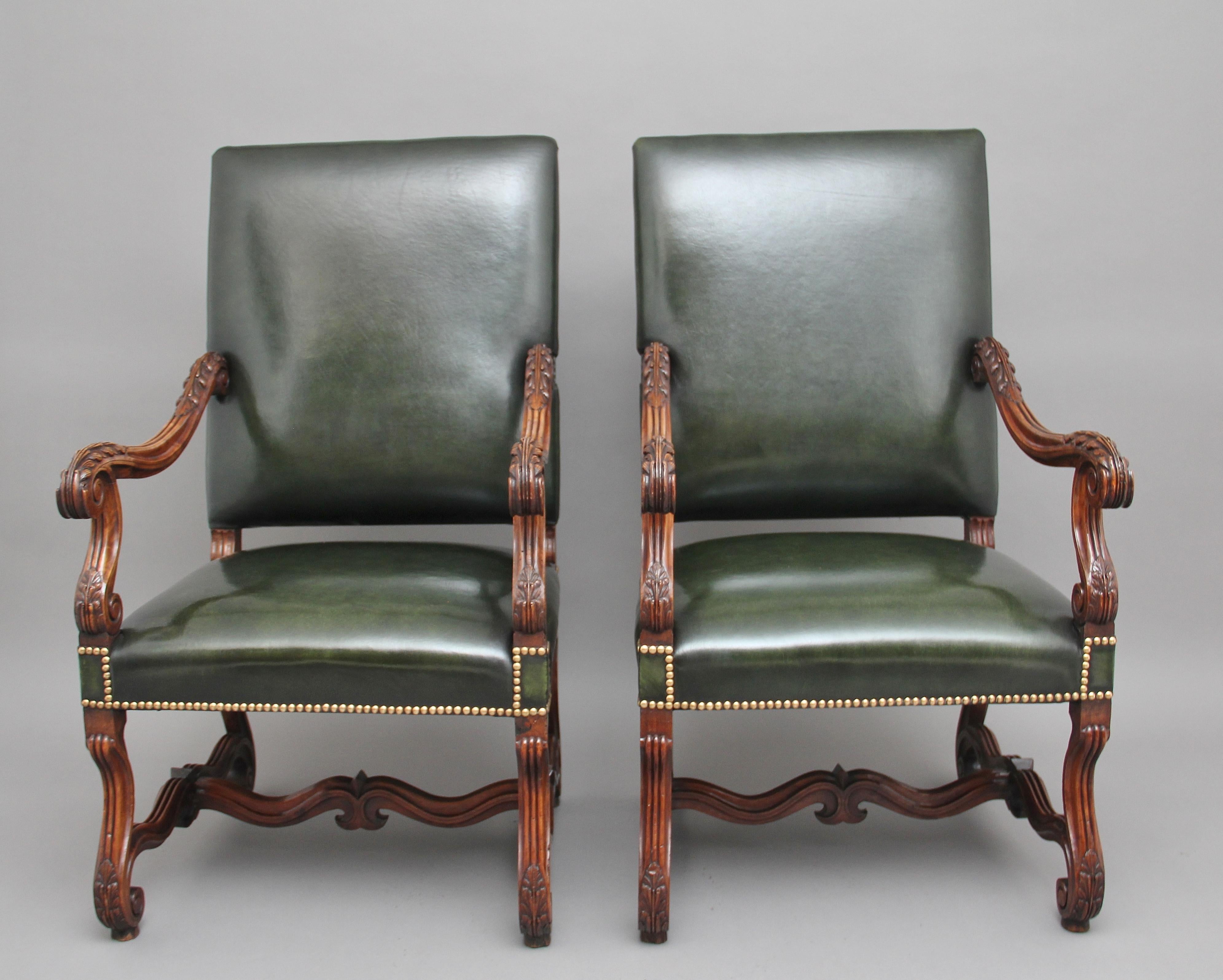 A superb pair of early 19th century French carved walnut armchairs, upholstered in green leather with brass stud decoration, shaped and carved arms with acanthus leaf decoration, supported on elegant shaped legs with carved scroll feet united by a