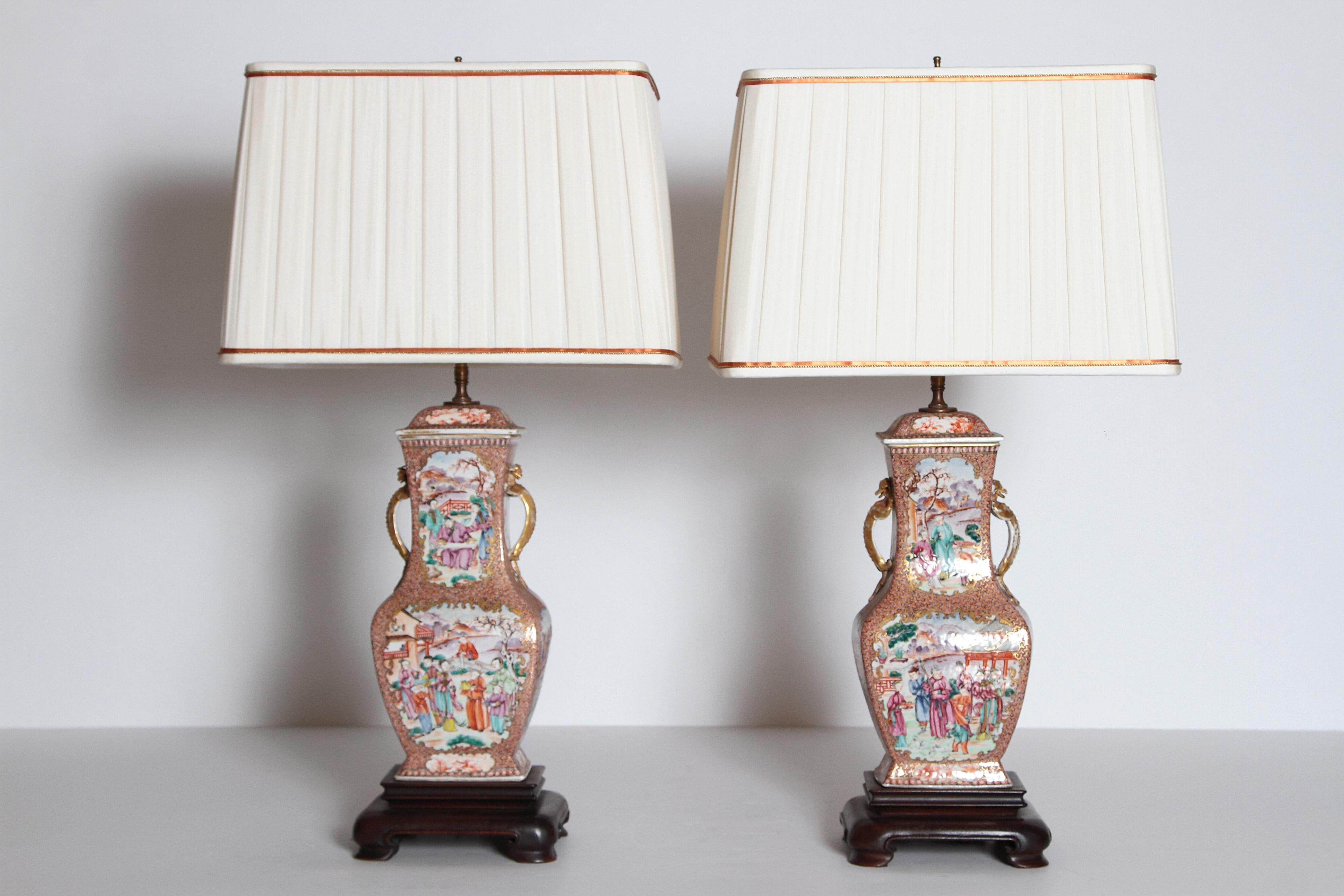 A pair of Chinese Export Rose Mandarin porcelain jars with lids as lamps. All four side have painted panels with people in landscapes on orange and gilt patterned background. A pair of gold lizards at the neck. Jars have been set on rectangular