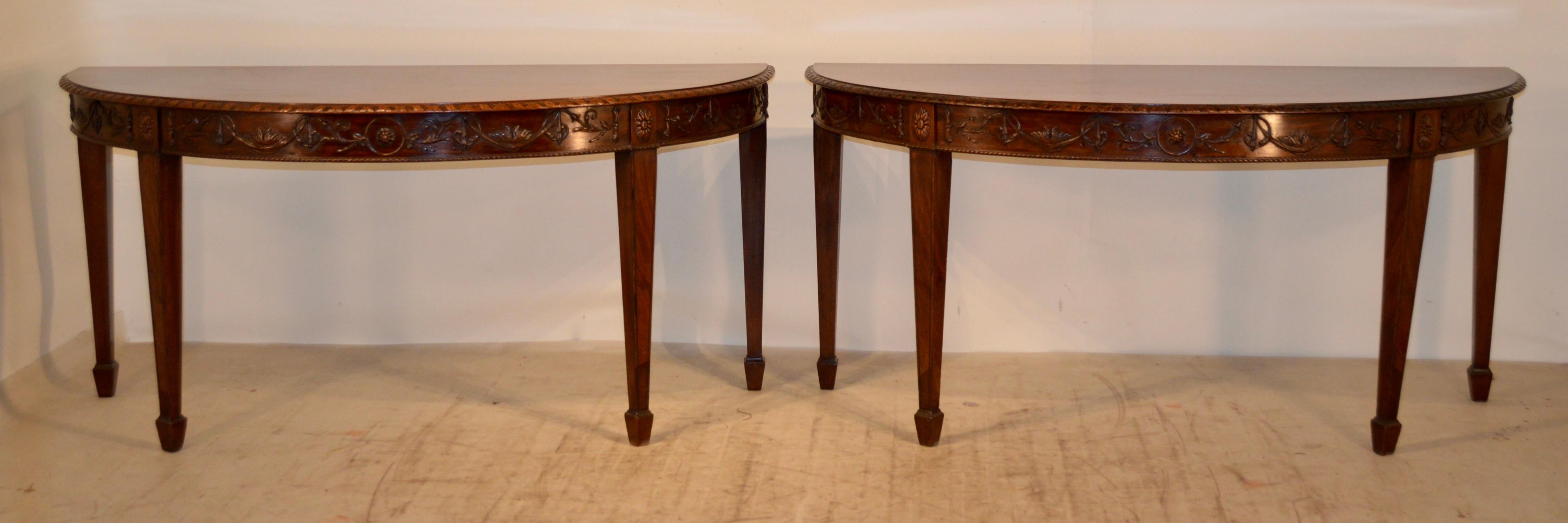 Pair of early 19th century mahogany demilune tables from England in the Adams style. The tables have hand carved decorated and beveled edges around the tops, following down to hand wonderfully decorated aprons with applied carvings, a few of which