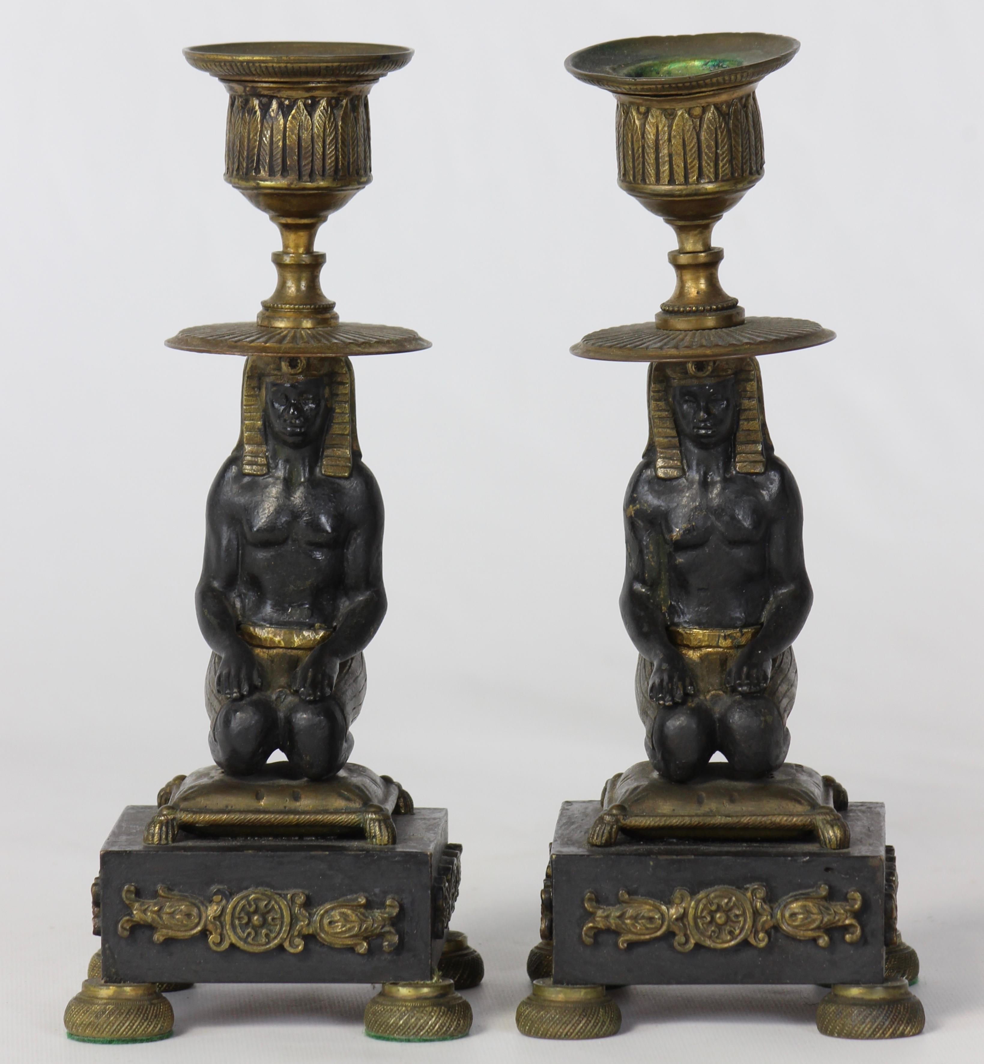 A pair of early 19th century French bronze figural Egyptian revival candlesticks depicting kneeling pharaohs on cushions.
