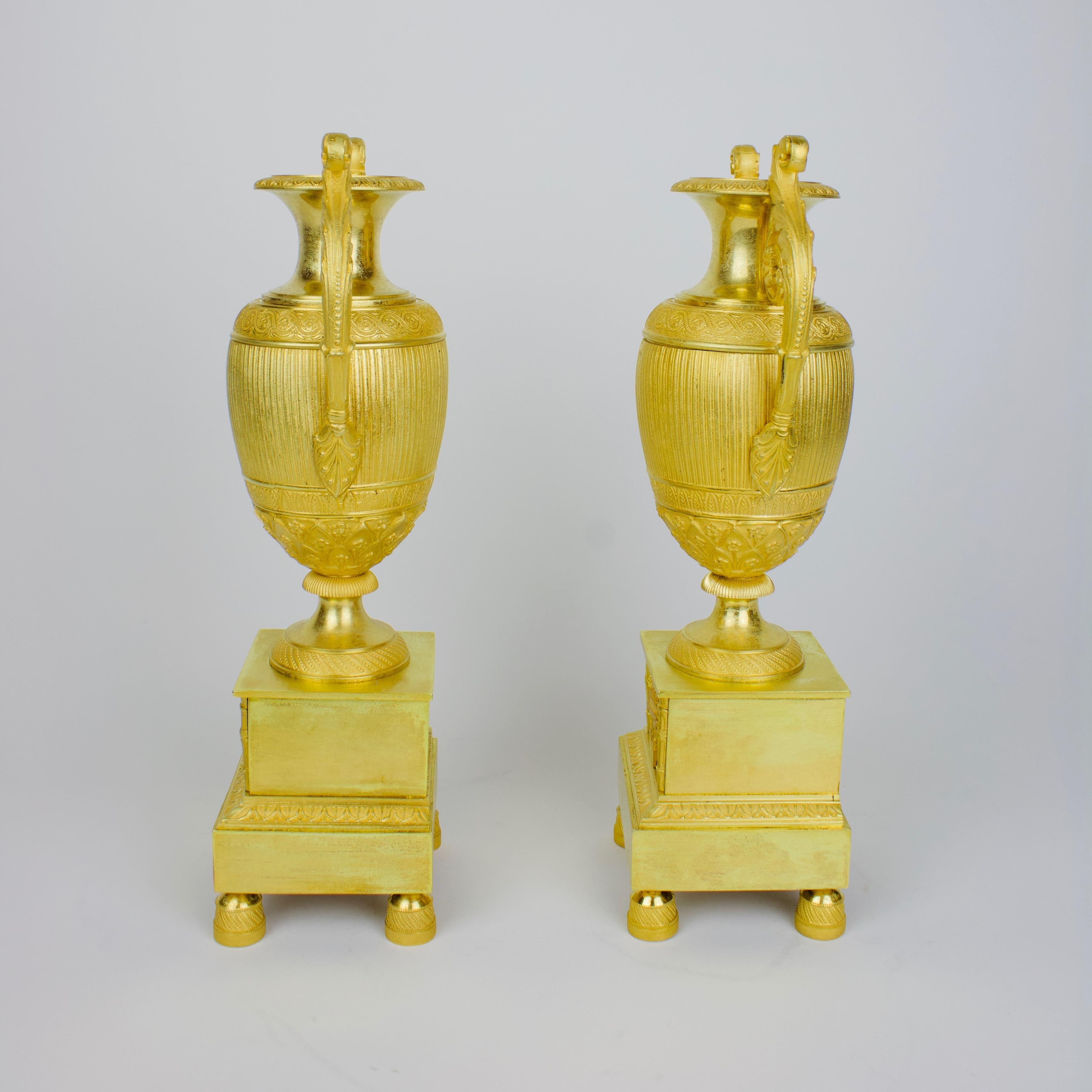 Pair of Early 19th Century empire gilt bronze neoclassical vases

Pair of early 19th century French Empire gilt bronze amphora vases:
each amphora vase with an ovoid fluted body and a round foot standing on a high rectangular pedestal with toupie