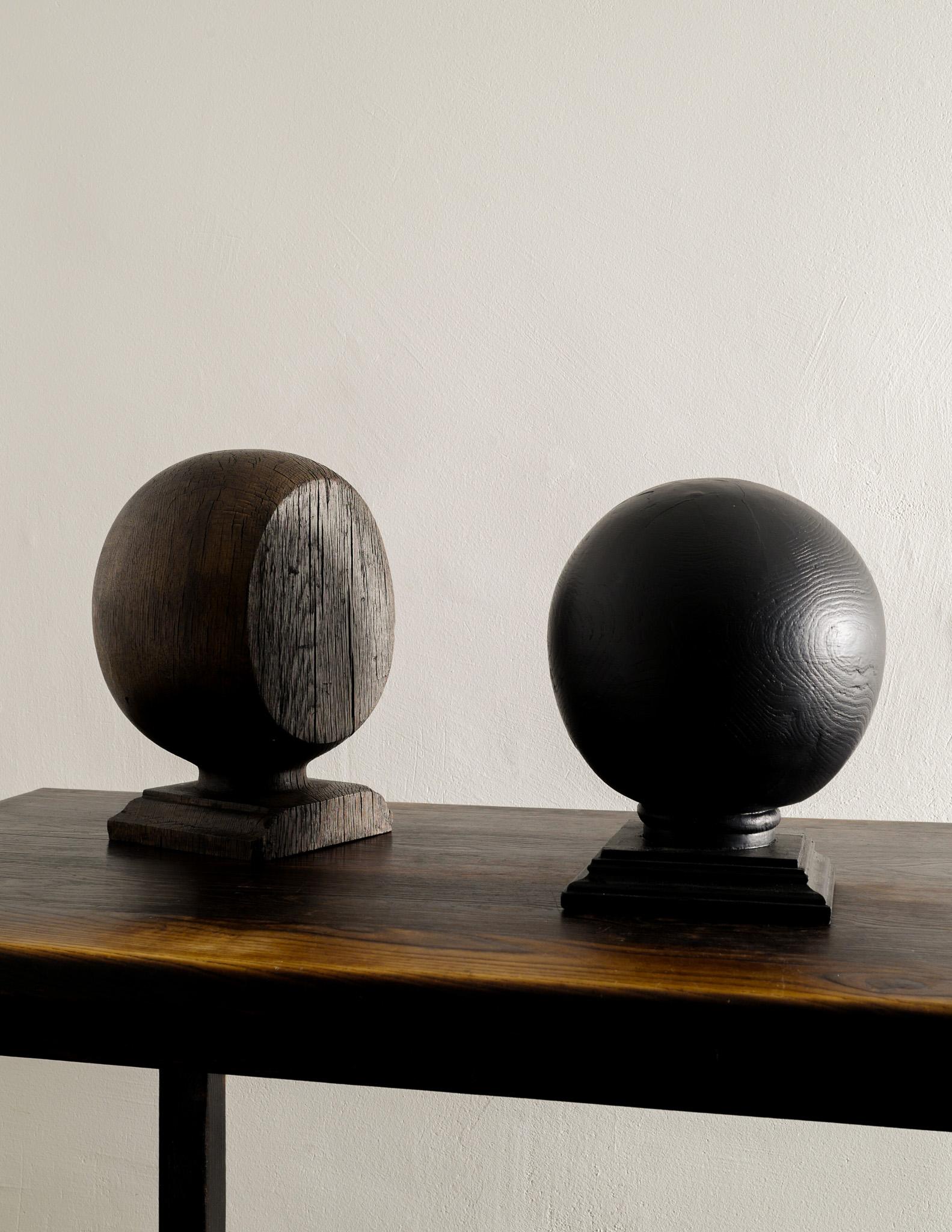Pair of British colonial wooden sculptural globes. The brown one is in solid oak and the black in stained pine. In great vintage condition and very decorative. 
Sold as a set. 

Dimensions: Brown: H: 39 x W: 29 x D: 25 cm Black: H: 34 x W/D: 36 cm 

