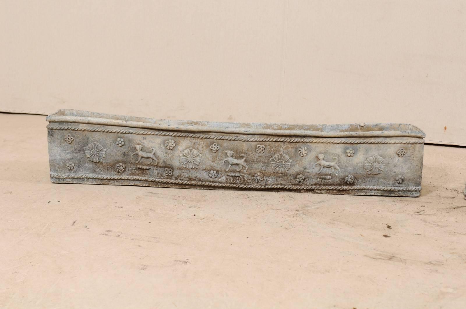 A pair of English early 19th century decorative elongated window boxes. These antique lead planter boxes from England are adorn on the front and two sides with prancing dogs and flowers, all surrounded within a roped trim outline. The back side of
