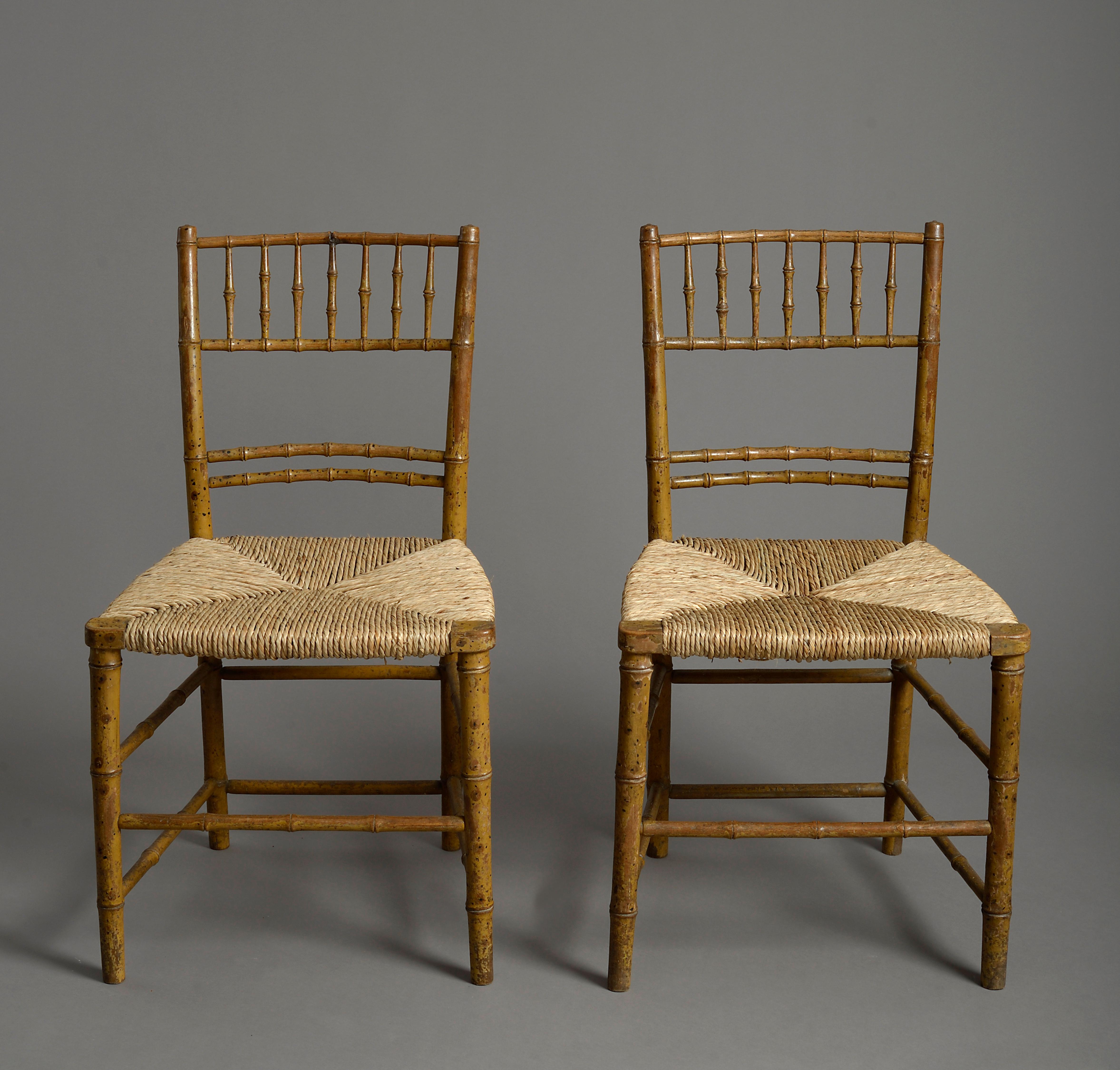 A pair of early 19th century Regency Period faux bamboo painted bedroom chairs, with spindle backs and stretchers and rush seats.