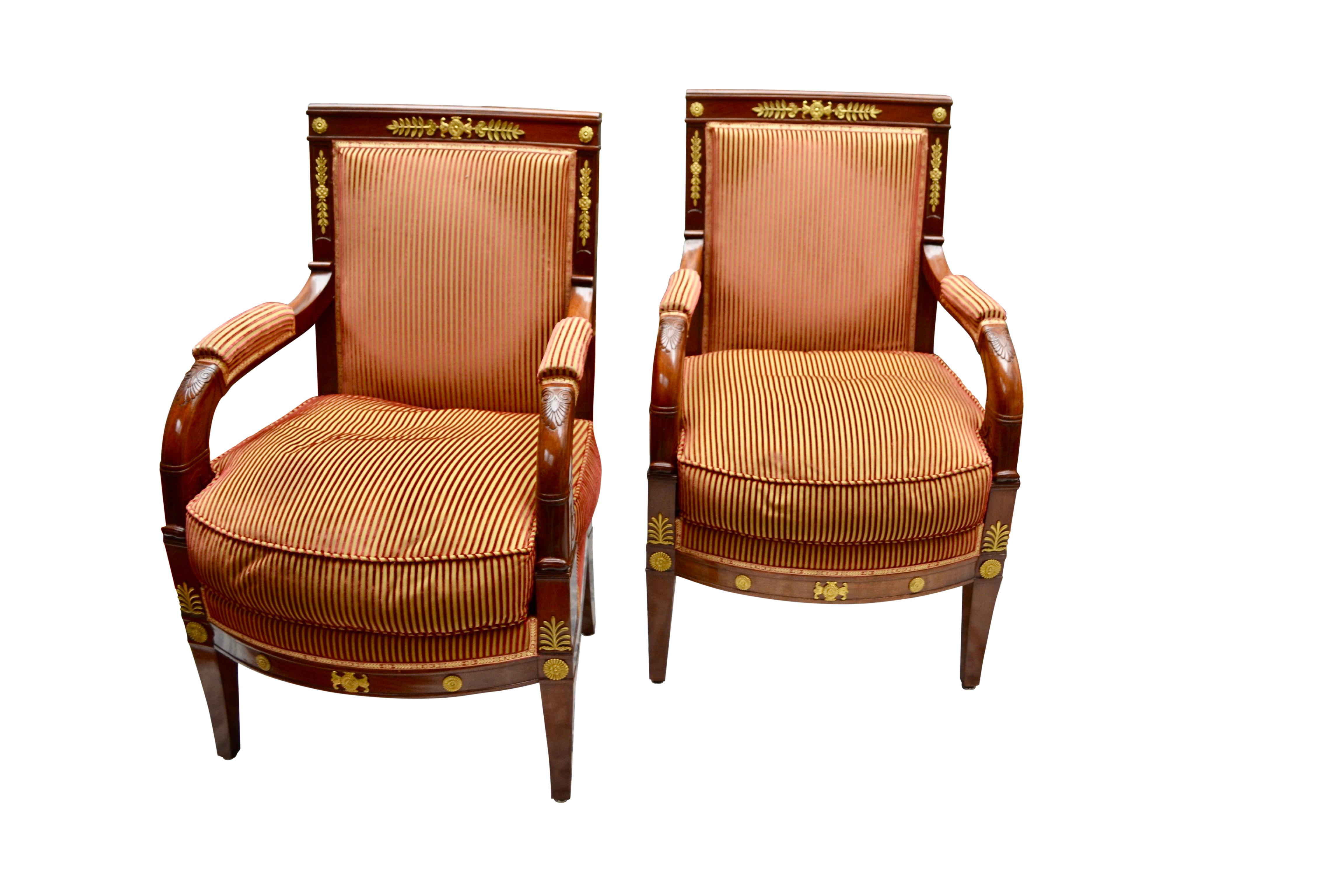A pair of French Empire mahogany fauteuils or armchairs 'a la Reine' in the manner of Jacob-Desmalter. The carved chair frames are in Honduran mahogany; the sloped padded open arms are carved with anthemions and continue into straight front legs;