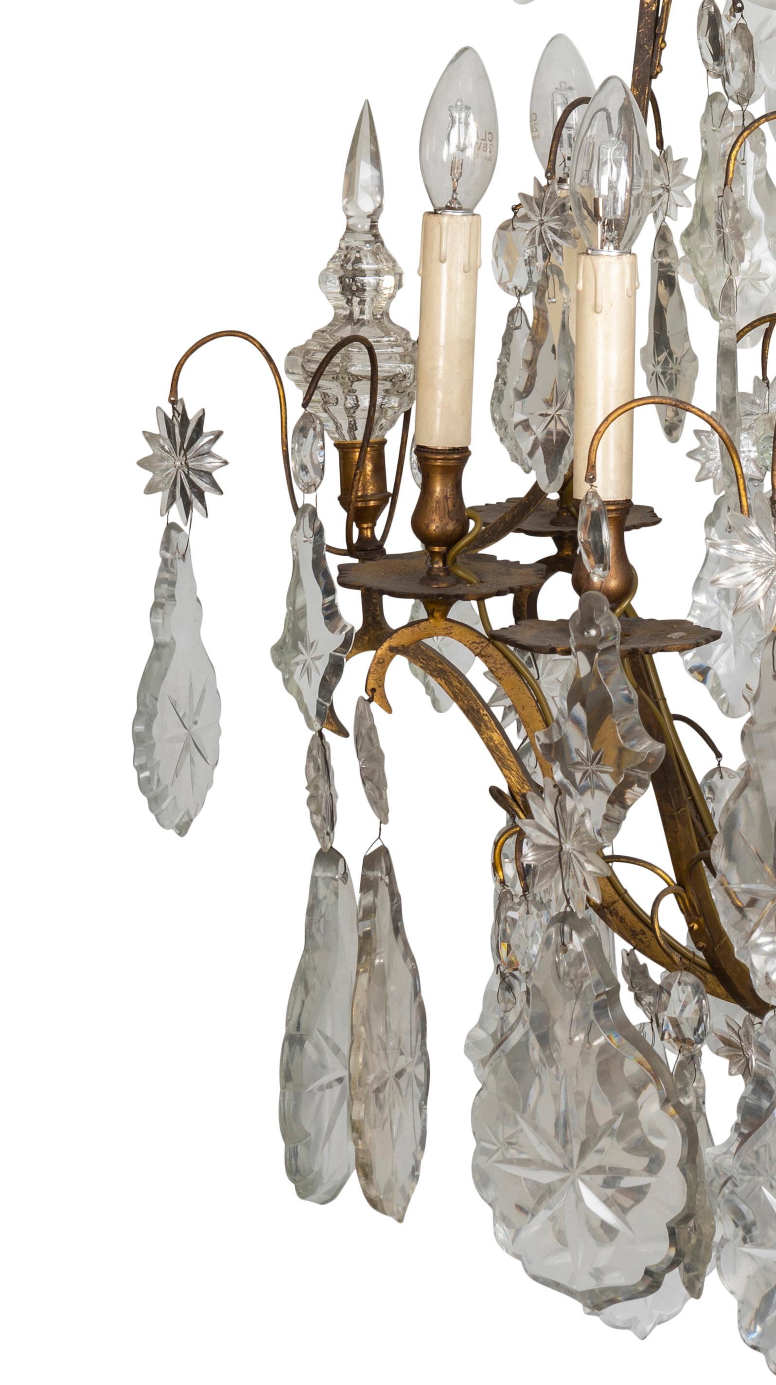 The pair of crystal and ormolu eight light chandeliers, each with a tendril corona to floral mount issuing four flat geometric arms, curving down to spire terminal on conjoined arms to lower mount with central baluster and spire vase terminal,