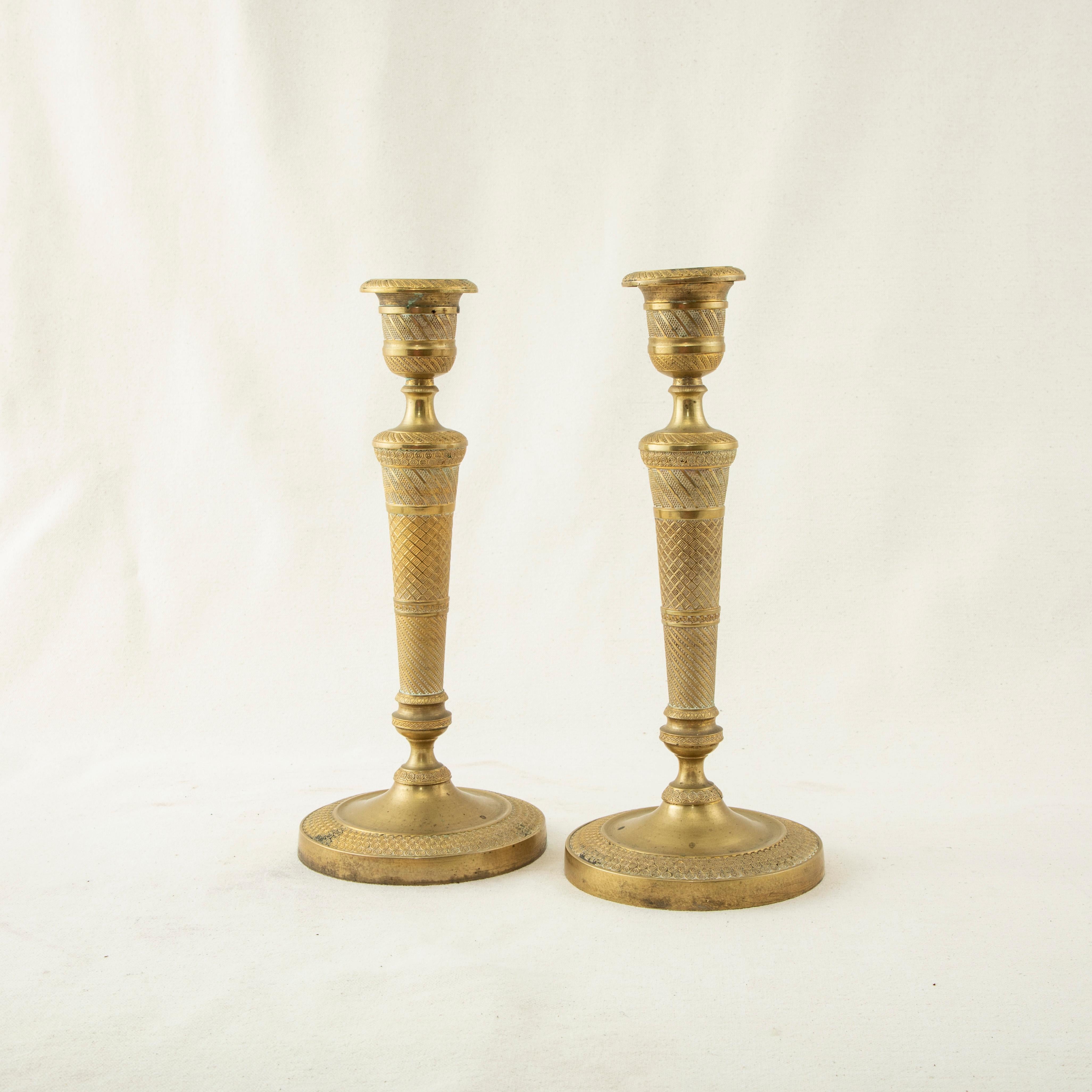 This pair of early nineteenth century French Restauration period bronze candlesticks features a spiral beading motif and concentric circle pattern. Each candlestick measures 10.5 inches tall by 4.5 inches in diameter at the base. The candlesticks
