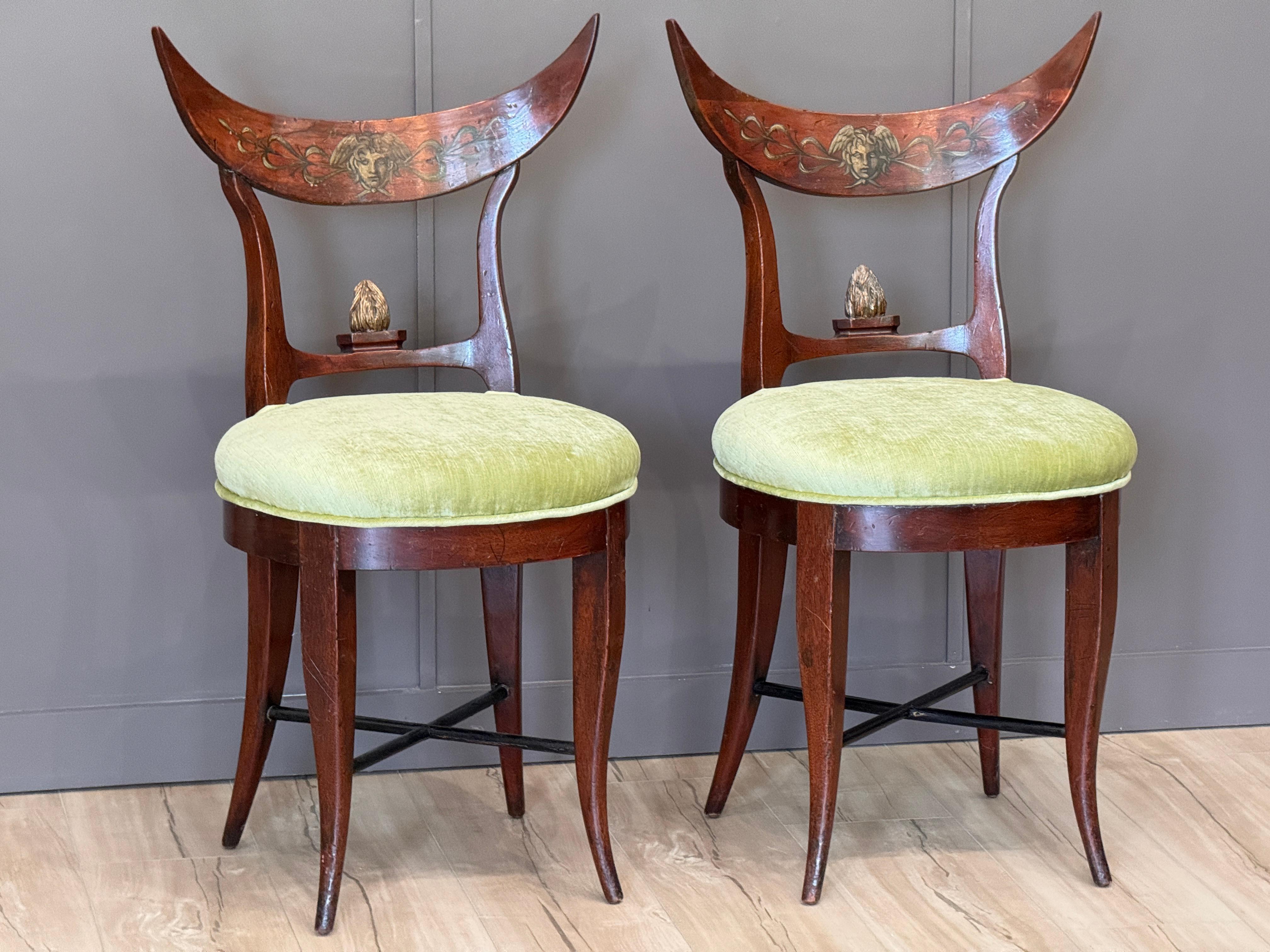 Coppia di poltroncine Beidermeier tedesche dell'inizio del XIX secolo, caratterizzate da binari a cresta curva dipinti con maschere femminili stilizzate e motivi a vite. Gli schienali scultorei si ergono su sedute rotonde generosamente imbottite in