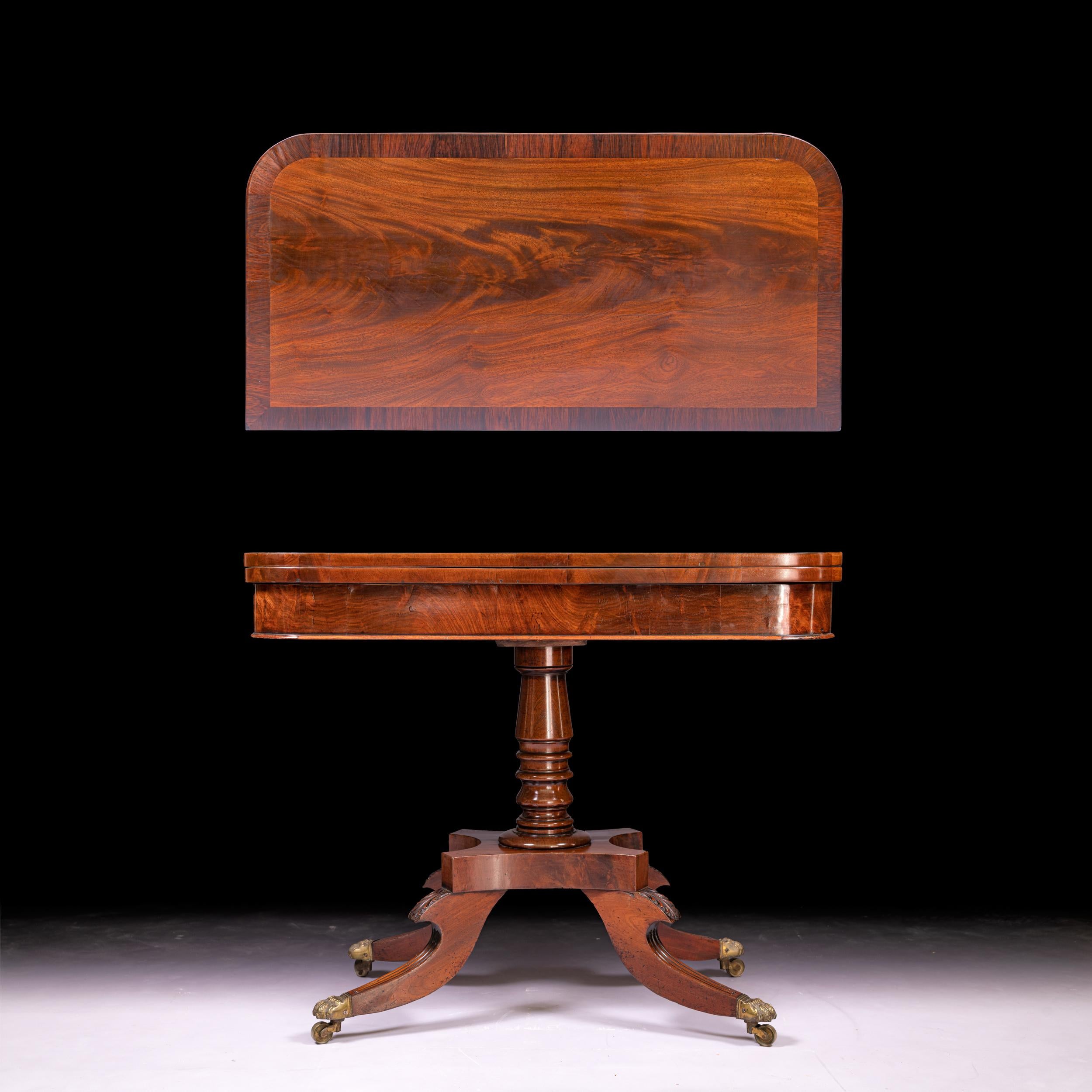 A pair of Irish Regency mahogany card tables, the rectangular top with rounded corners and a swivel-hinged top, enclosing a green baize inset playing surface, each frieze with a rectangular panel, raised on a baluster column, terminating on outswept