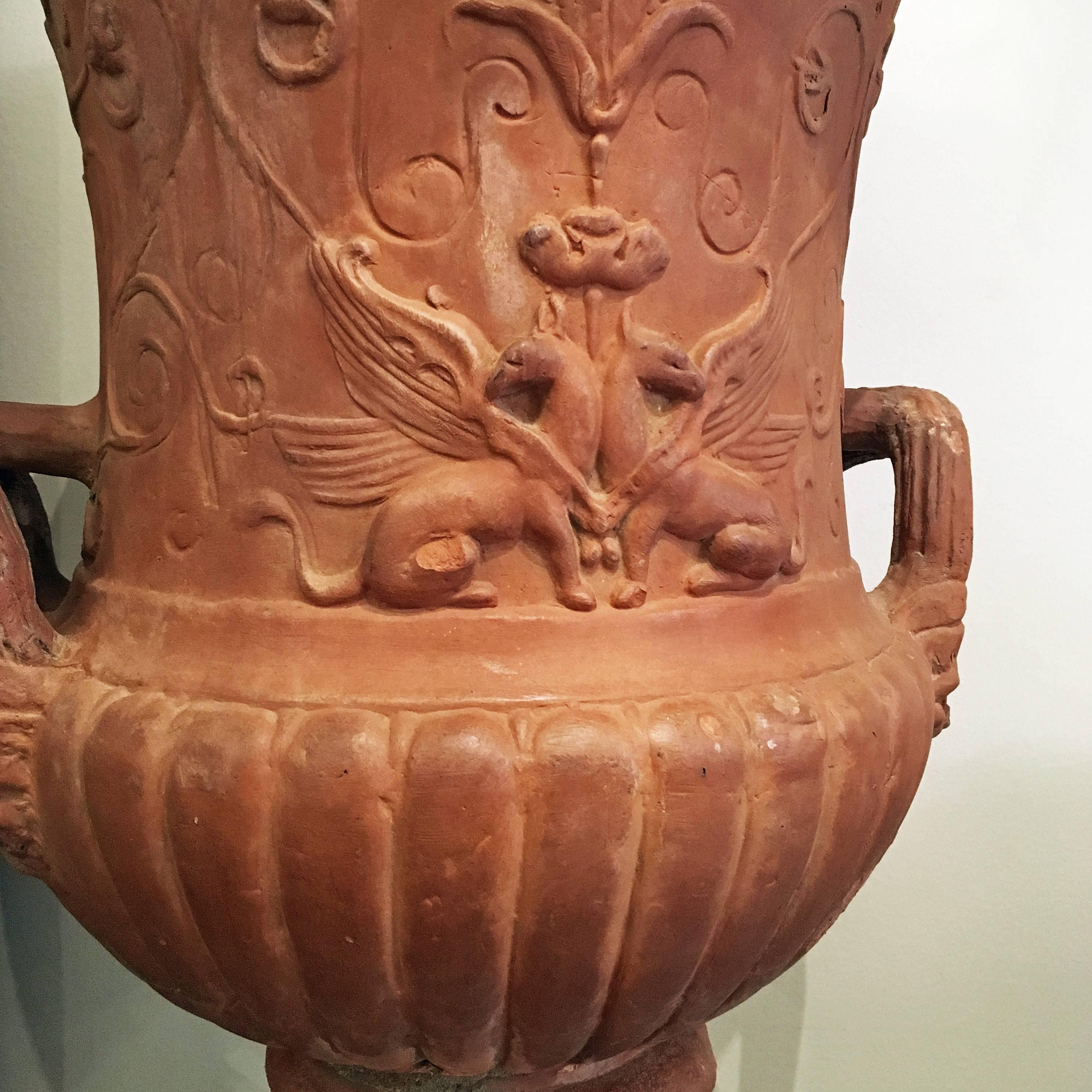 An elegant pair of Tuscan neoclassical Medici style terracotta urns. The square plinth is surmounted by a fluted circular base and the main body with two large handles. The surface of the urns is decorated with reliefs depicting foliate motifs,