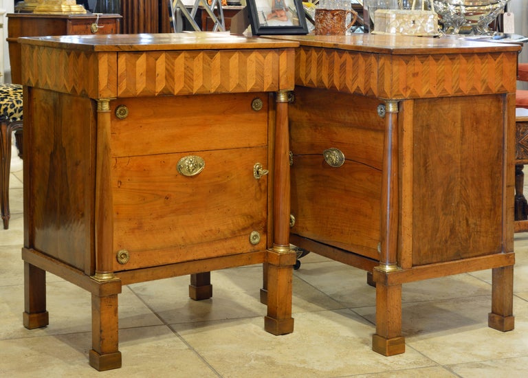 This lovely pair of Italian neoclassical commodes feature a fetching arrow parquetry frieze with one drawer above a bronze accented door opening up to a one shelf interior and flanked by classical style columns with bronze mounted capitals and