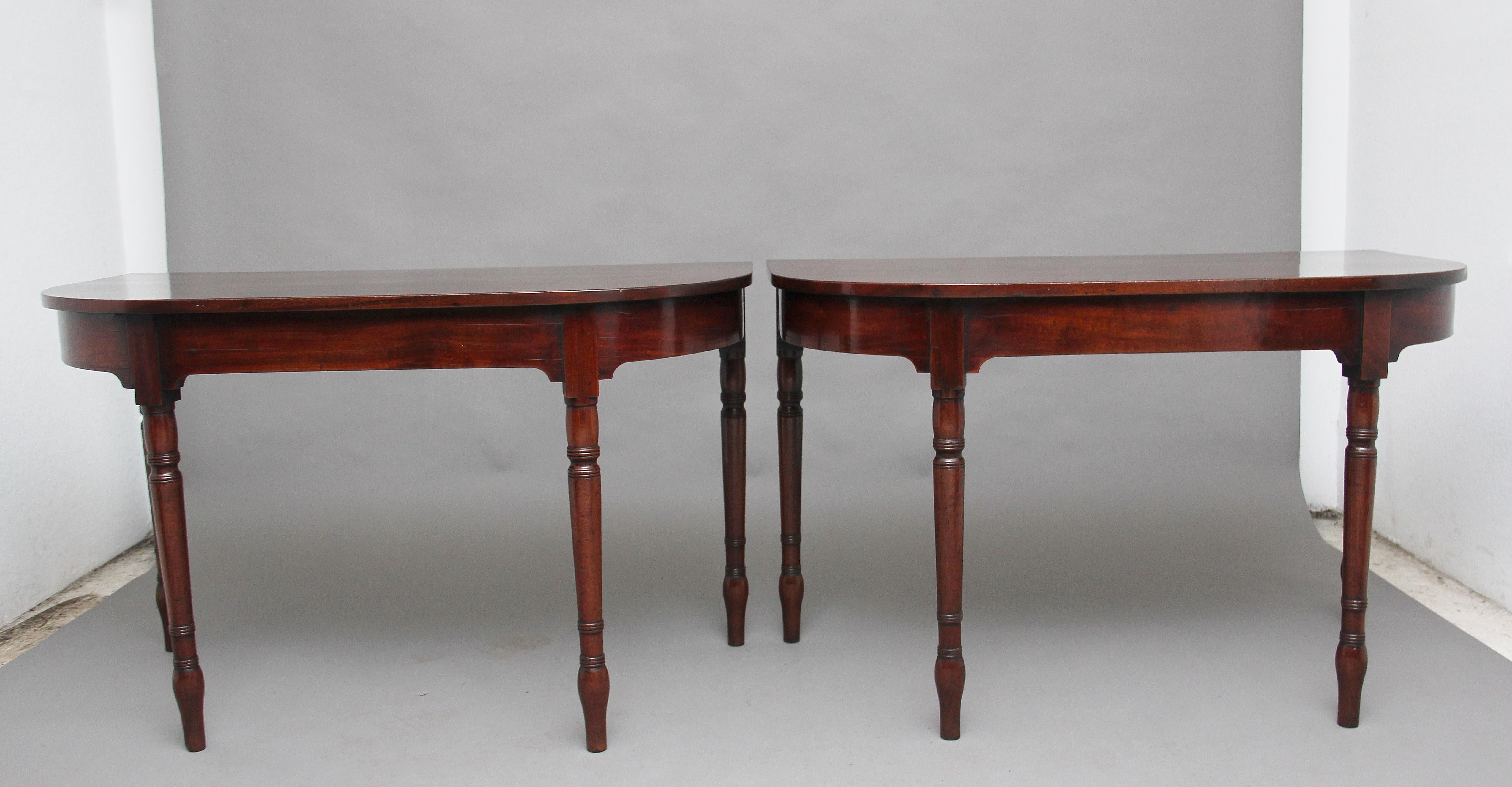 A pair of early 19th century mahogany console tables, the wonderfully figured demilune shaped top above a shaped apron, supported on elegant turned legs. The tables have a lovely nice warm rich mahogany color and both are in excellent condition,