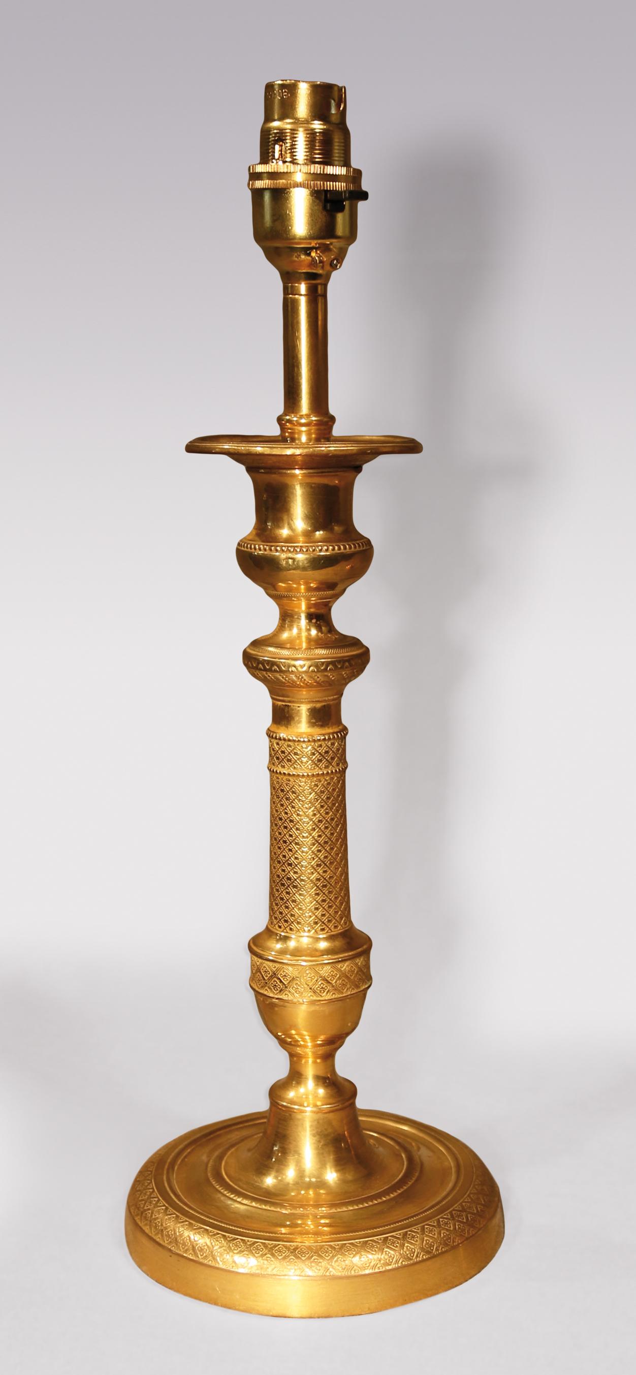 A pair of early 19th century ormolu candlesticks, having urn-shaped nozzles above vase and columns stems ending on circular bases. (Now converted to lamps). Measurements with shade H 18.5