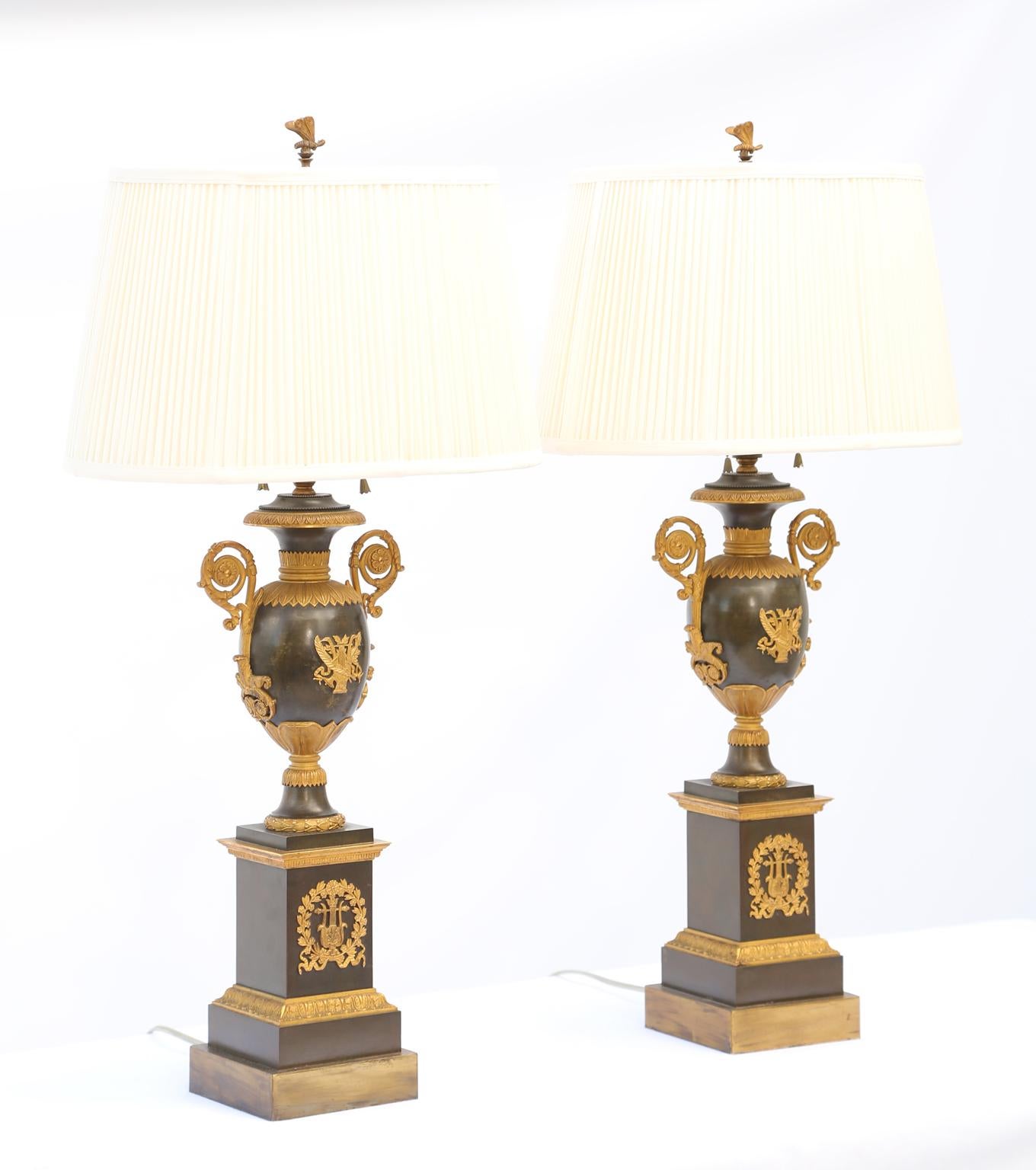Fine pair of period Empire table lamps, of gilt and patinated bronze, each having an urn, centered by a lyre, ribbons, and laureling, its foliate-chased neck and shoulder are flanked by elaborate scrolling handles centered with a rosette,
