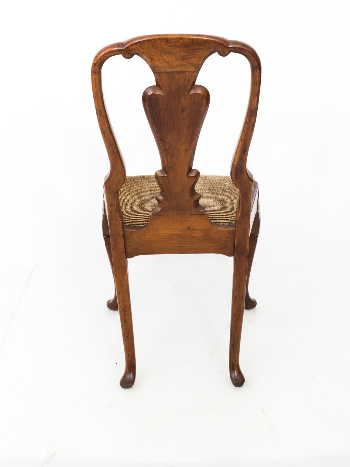 Circa early 19th century pair of English Queen Anne side chairs with upholstered seat and pad feet. The chairs also feature a vase-shaped back splat and cabriole legs with carved knees. Please note of wear with age including indents in the wood. 