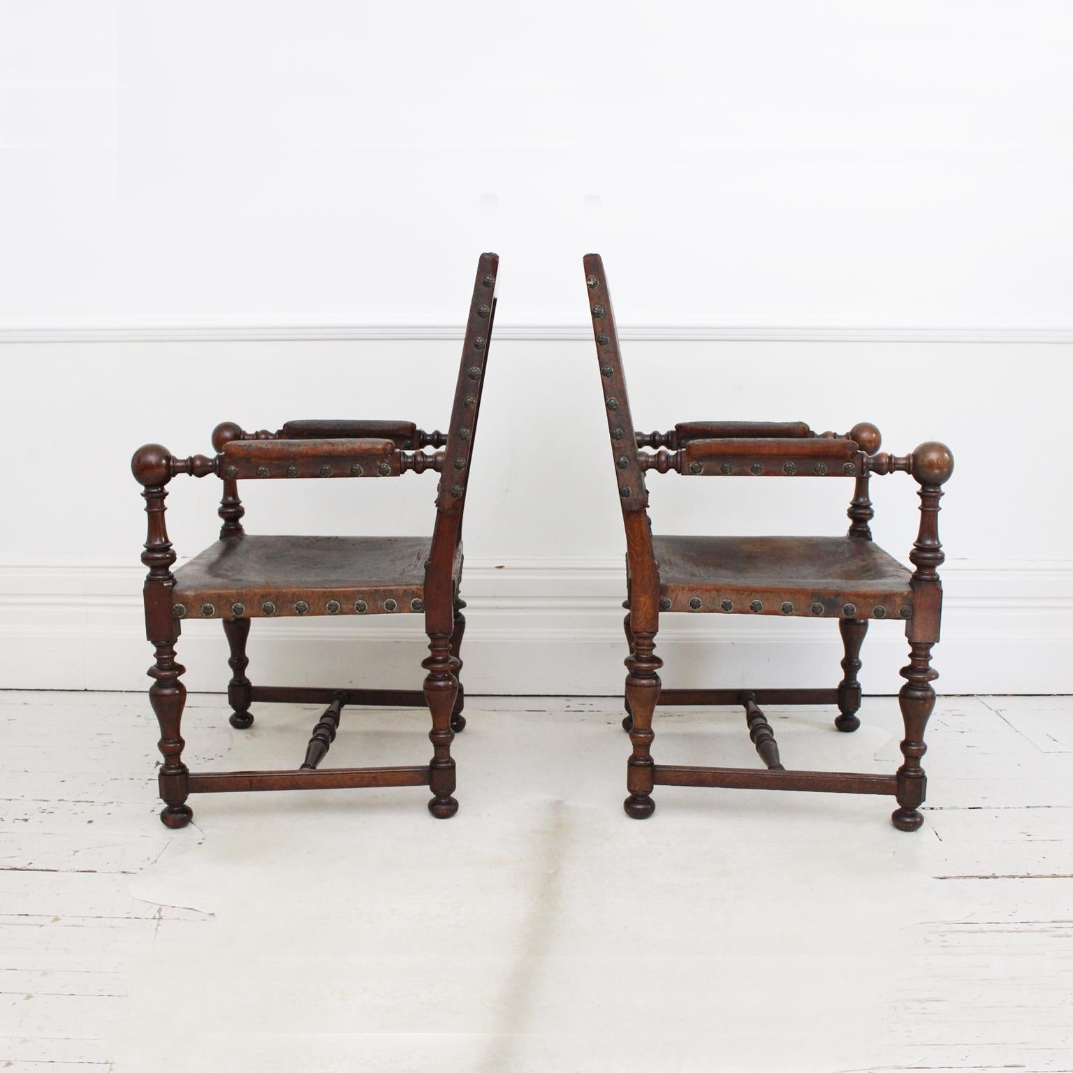 This magnificent, large pair of oak armchairs retain their original, beautifully worn and embossed brown leather. They are profusely turned throughout. The leather is scalloped and studded, the oak has a good color. These would look great at the
