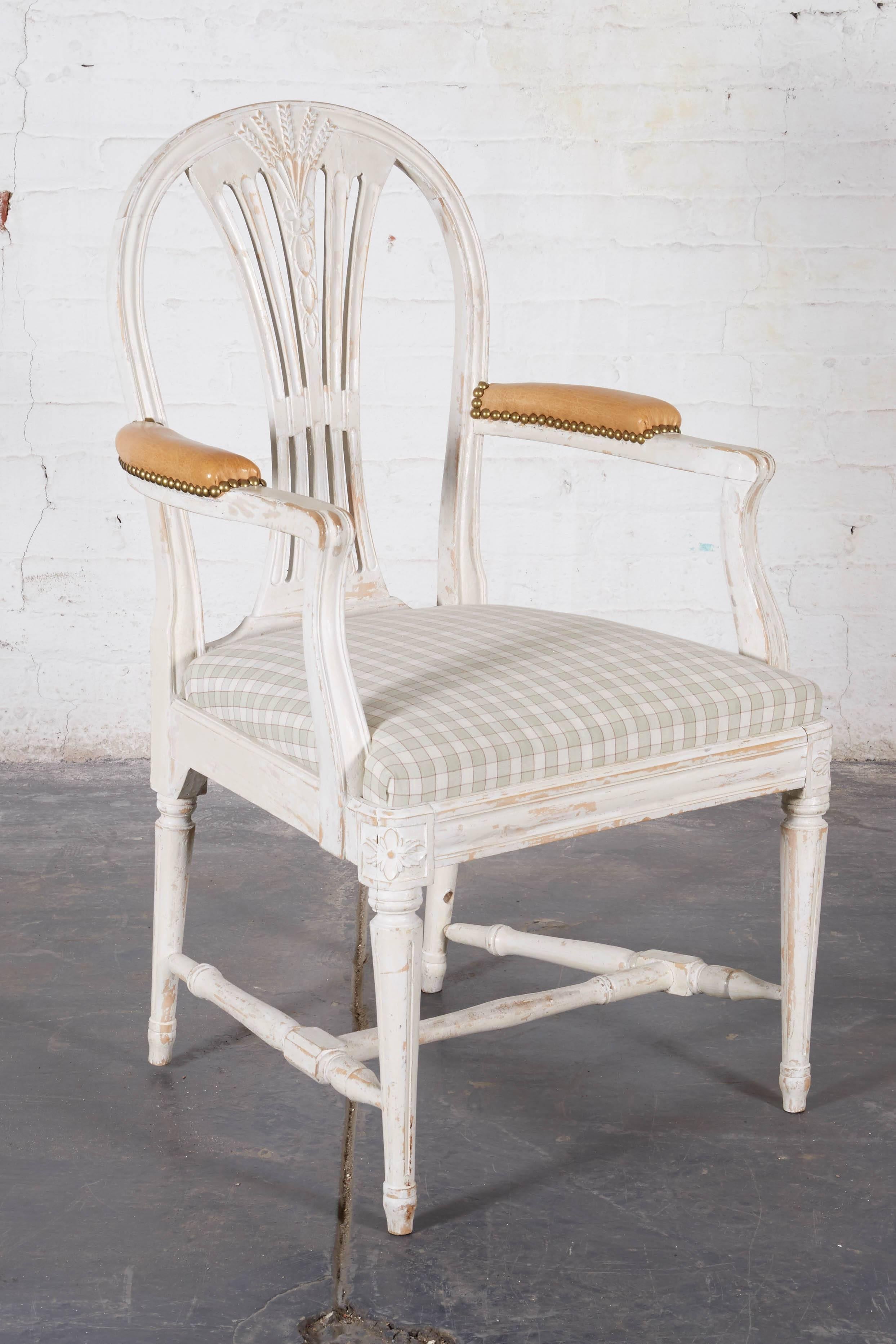 Conceived in the Sheraton/Hepplewhite style with arched back centred by a pierced backsplat with wheat sheath decoration; the armrests with tan leather manchettes; the drop-in seat upholstered in a cotton check; raised on turned tapering legs joined