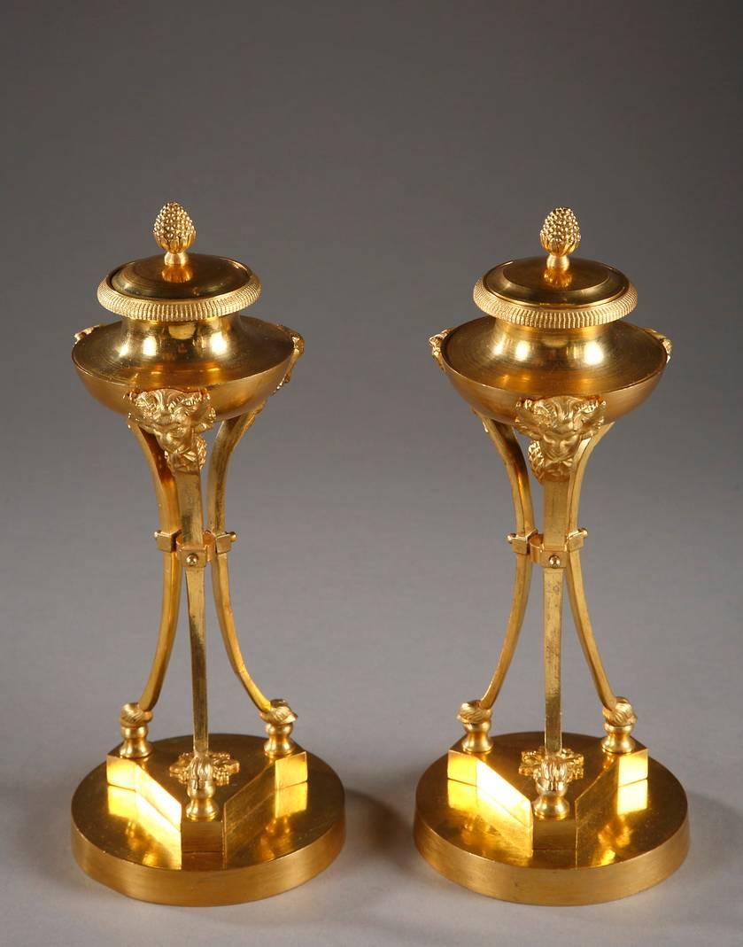 Pair of gilt bronze tripod candlesticks, composed of a circular base supporting three incurved pilasters decorated with satyr heads. A vase inspired by Antiquity rests on the heads of the satyrs. The vase cover is delicately carved with laurel