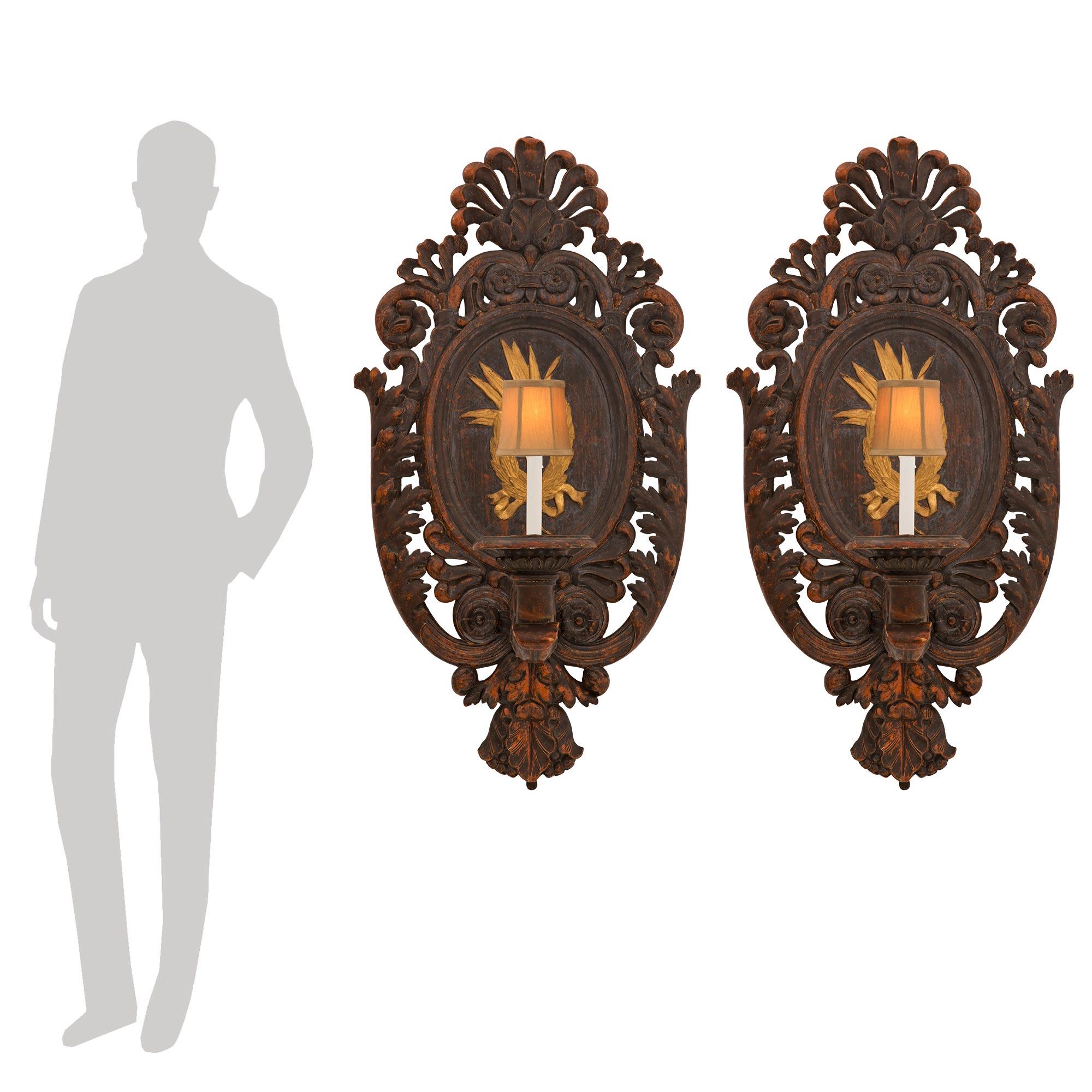 A handsome and monumentally scaled pair of Italian early 19th century Baroque st. polychrome and giltwood sconces. Each impressive sconce is centered by a richly carved pierced bottom foliate design below striking large scrolled foliate movements