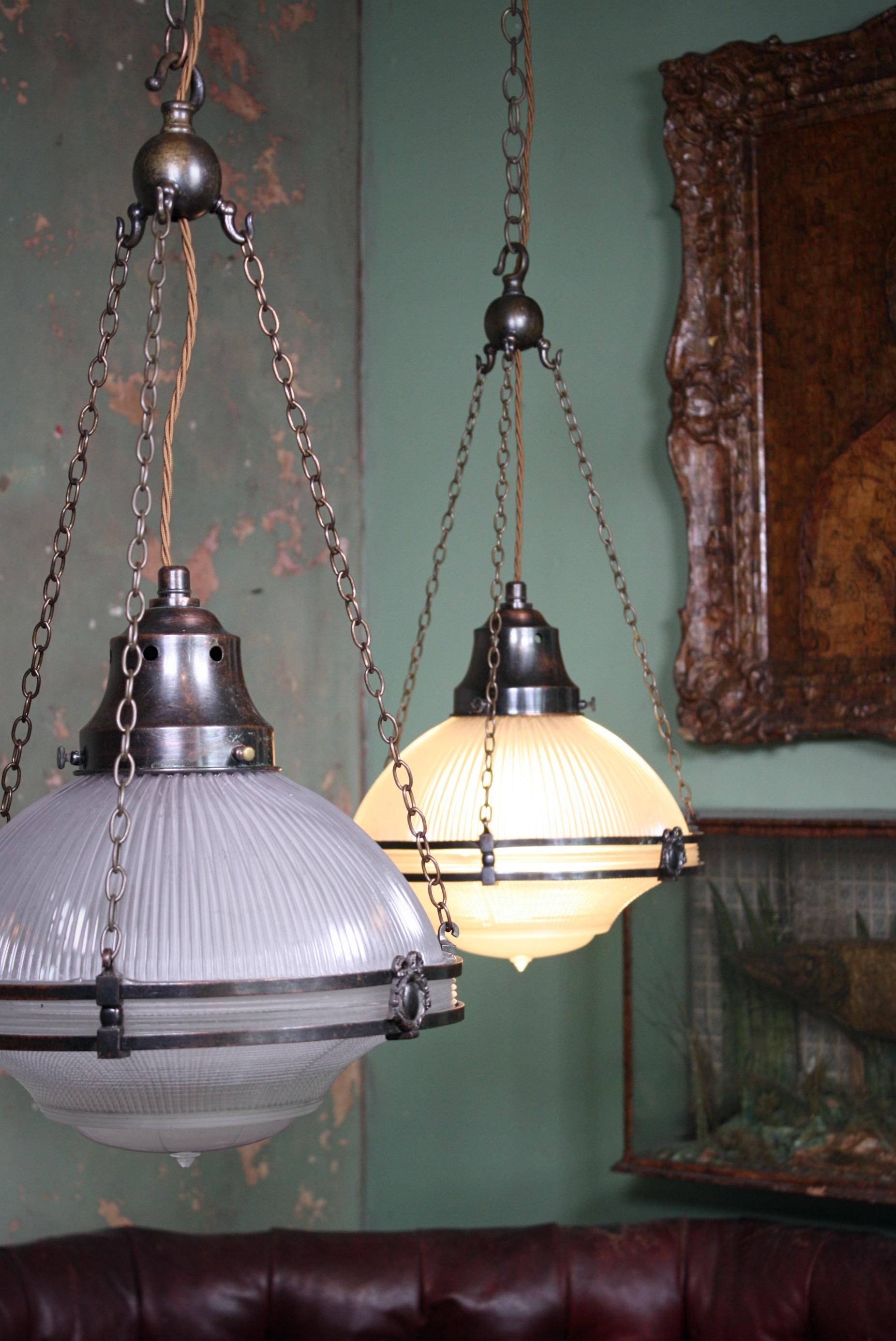 An elegant pair of Holophane single chandeliers, three sections of prismatic glass sits within a bronze cage with original galleries, chains & four way hanging ball.

All metal section has age related oxidization, each like comes with a length of