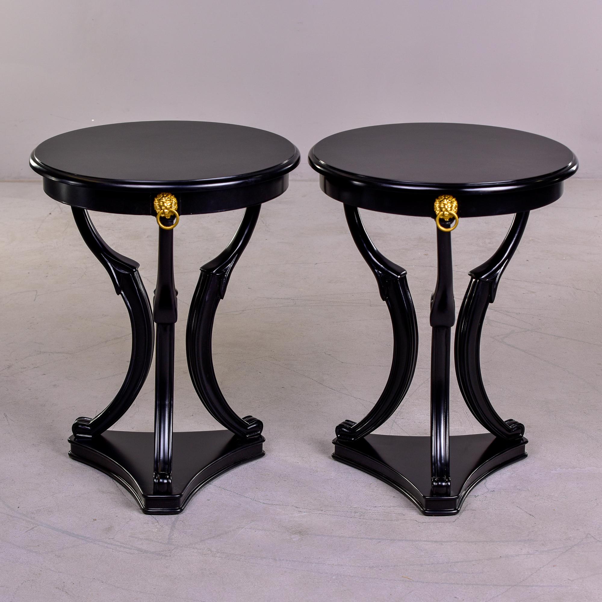Pair of circa 1920s French neoclassical style guerdon side tables with new black painted finish, triangular base, three carved and curved legs, round tops and decorative gold lion’s head mounts. Unknown maker. Sold and priced as a pair.
 