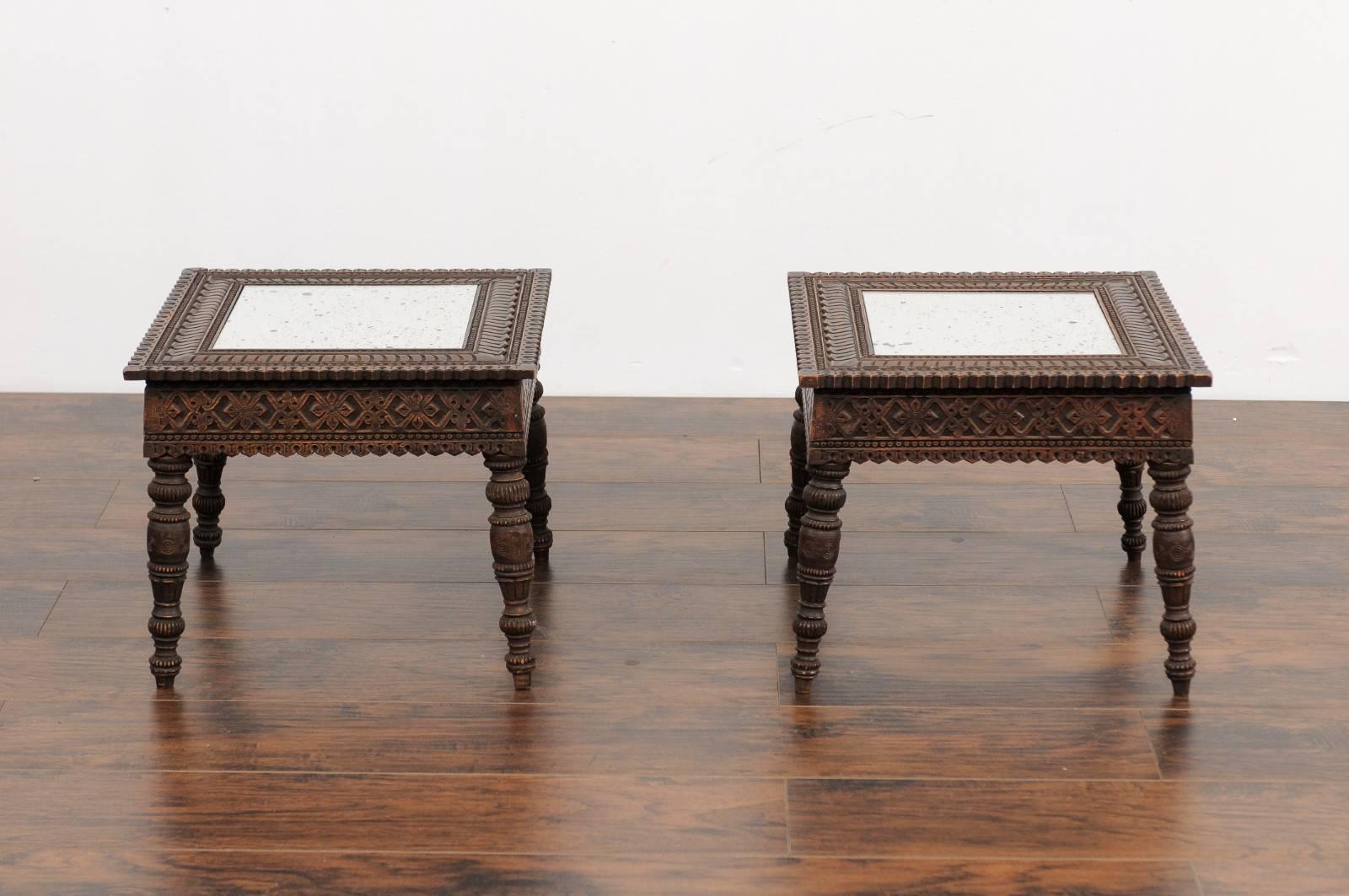 A pair of Anglo-Indian carved wood drink tables from the early 20th century with new antiqued mirrored tops. Each of this pair of side tables features an exquisite rectangular top, skilfully carved with various motifs surrounding a central