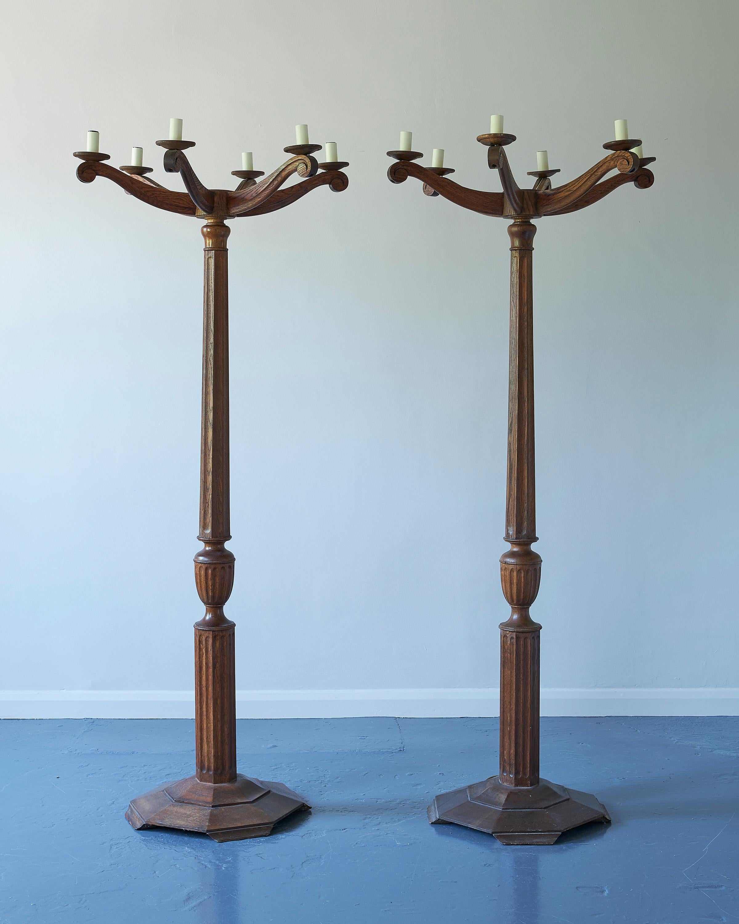 A matching pair of Art & Crafts candelabra floor lamps, early 20th century, solid oak, each with six arms and sconces, the reeded shaft with fluted baluster section, octagonal bases, electrified.