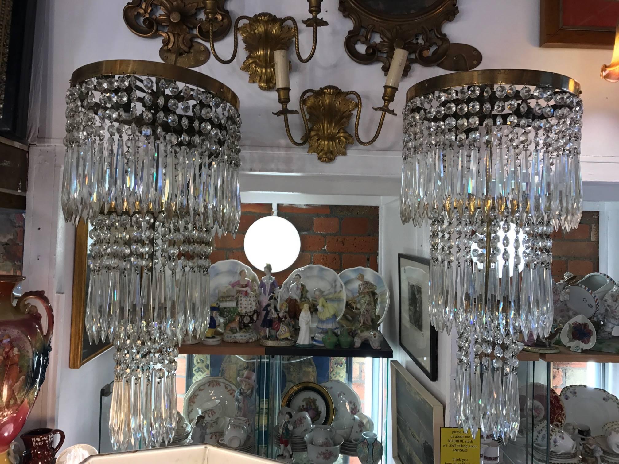 A pair of early 20th century articulated crystal wall sconces, Three tears of crystal drops held on a smile brass surround. The wall fixture is simple and hidden.