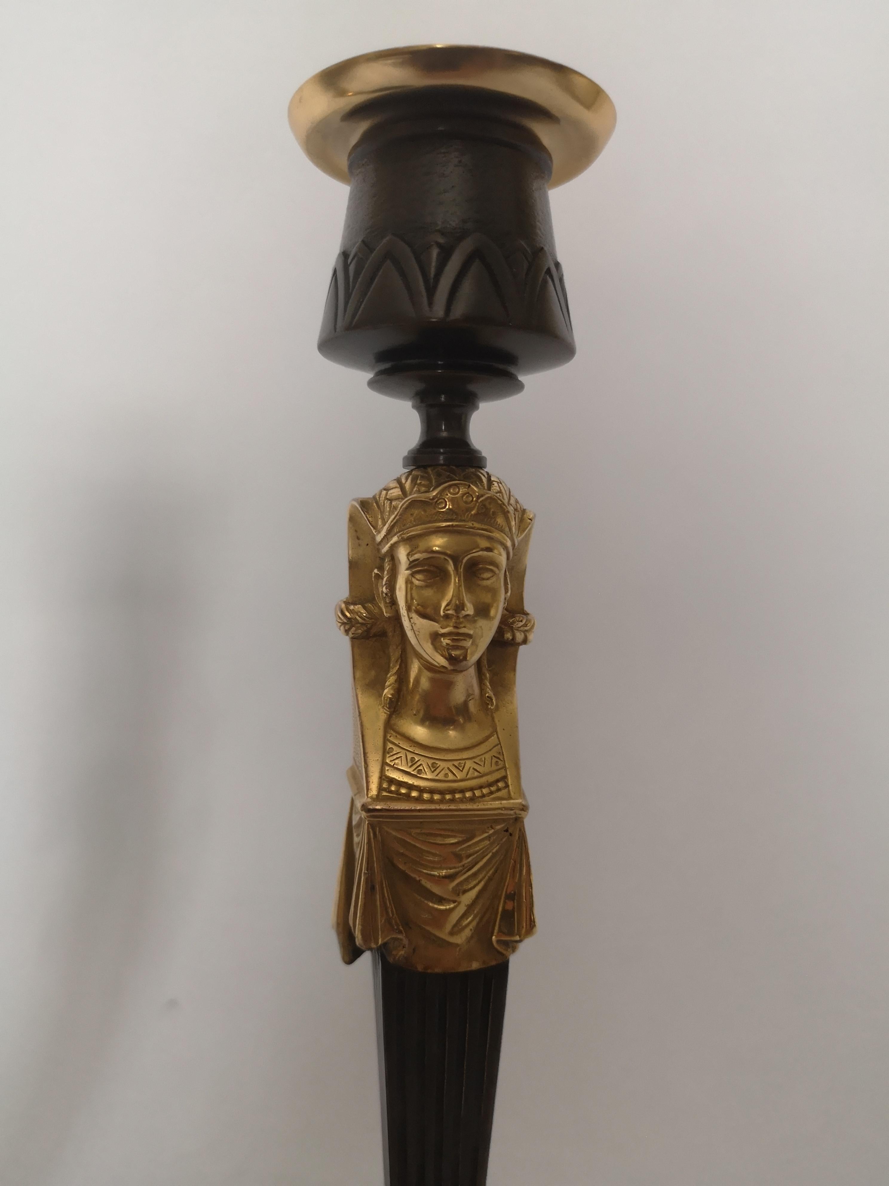 A pair of early 20th century candlesticks in the Egyptian taste. Each decorated a gilt pharaoh's head below the sconces and leaf decoration to the base,
French, circa 1920.