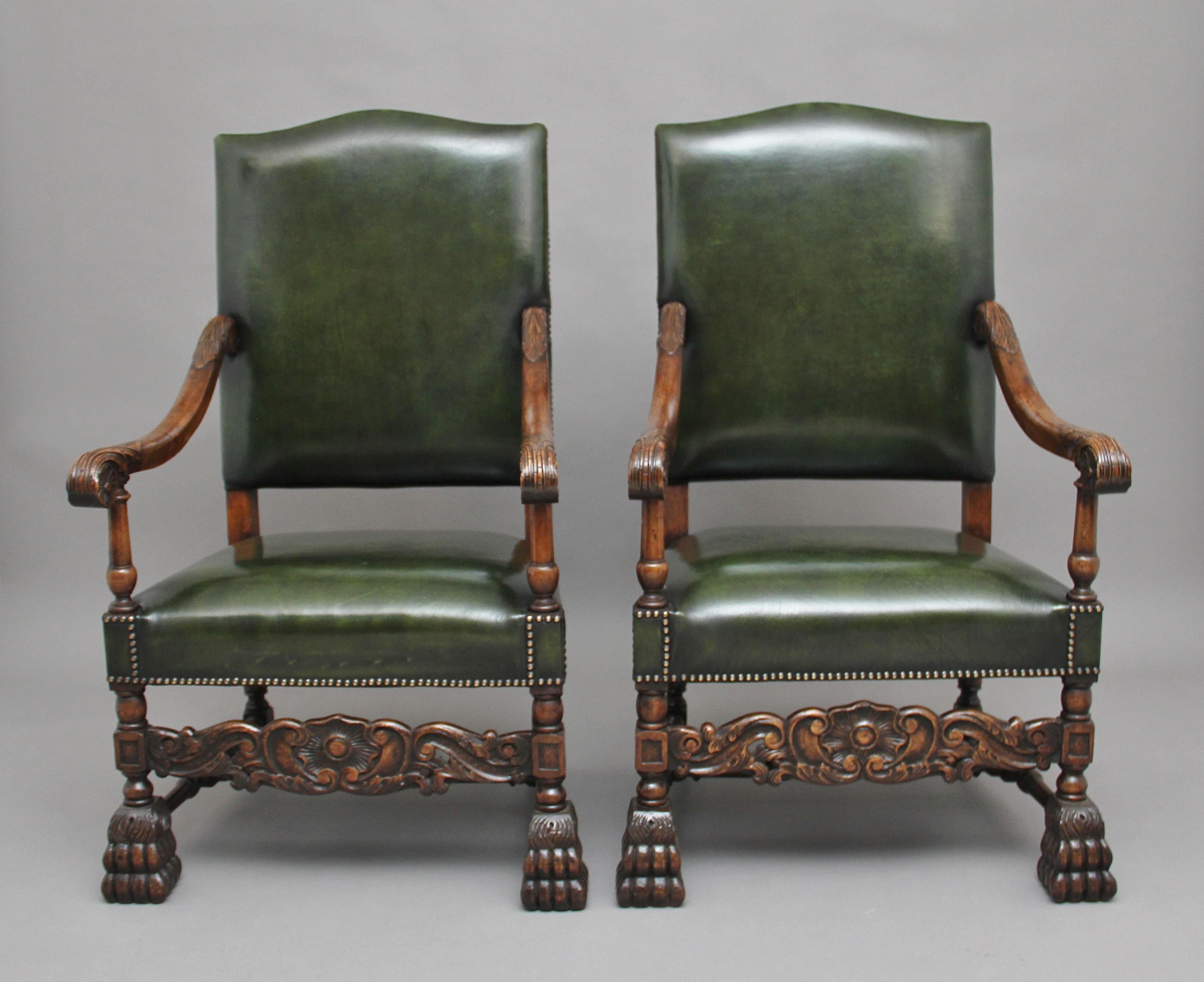 A decorative pair of early 20th century carved armchairs in the Carolean style, upholstered in green leather with brass stud decoration, shaped and carved arms with acanthus leaf decoration with finely turned arm supports, standing on bold carved