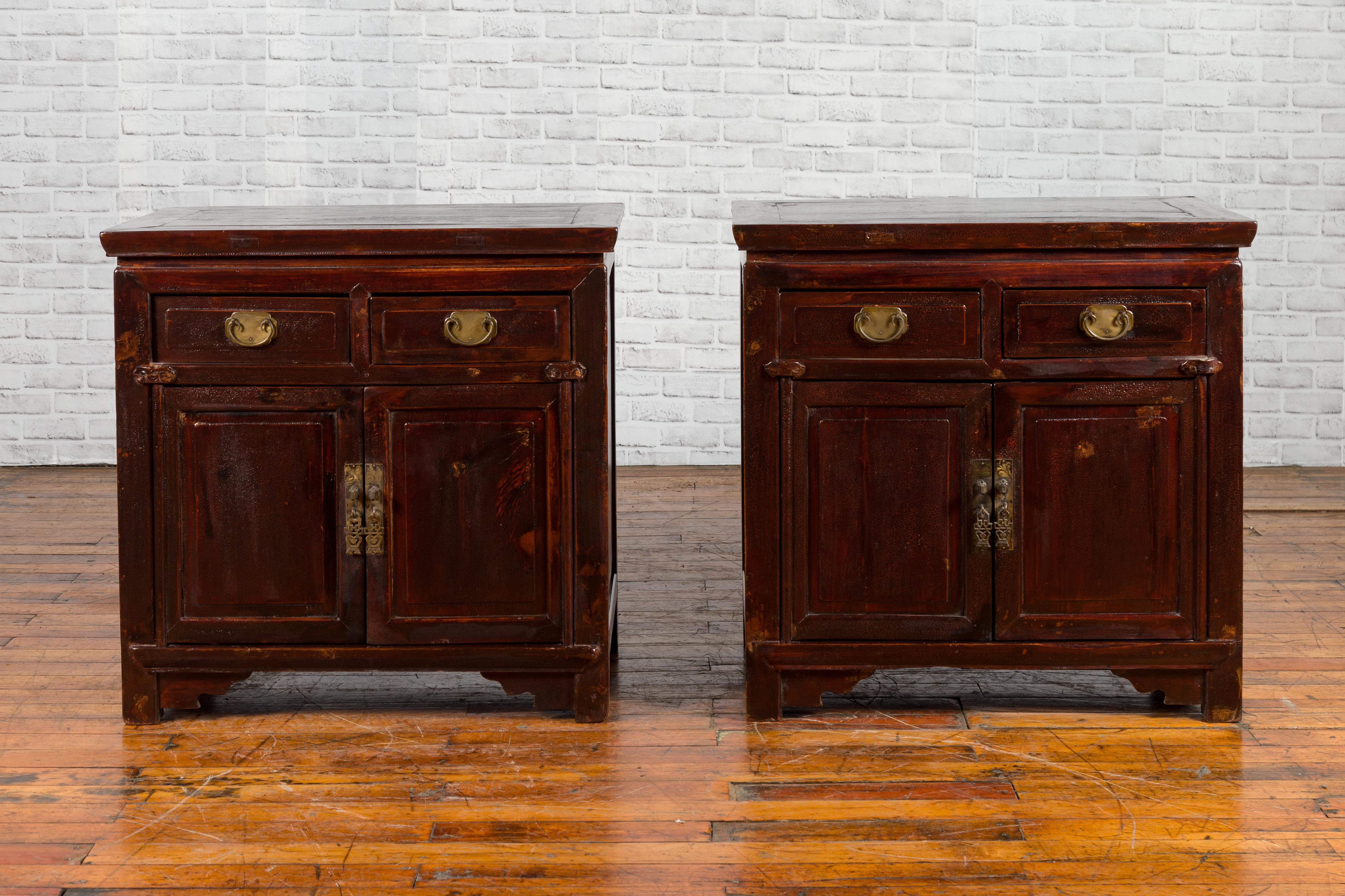 A pair of Chinese antique bedside cabinets from the early 20th century, with drawers, doors, brass fittings and reddish brown lacquer. Created in China during the early years of the 20th century, each of this pair of bedside cabinets features a