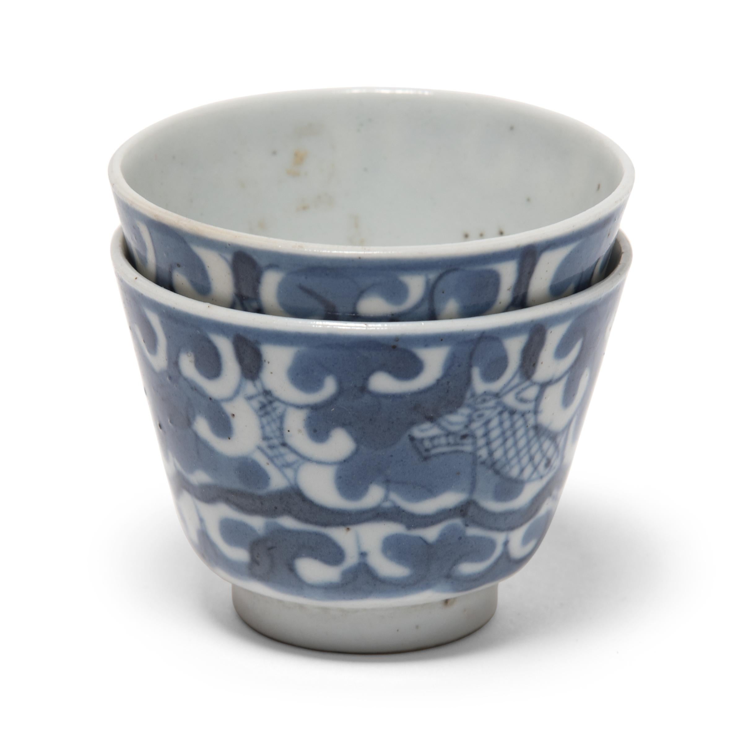 The blue and white design of these porcelain teacups was painted in a muted, grey pigment, only to be transformed to a rich, cobalt blue by the fiery heat of the kiln. Painted with a simple cross-hatch pattern, a serpentine dragon weaves its way