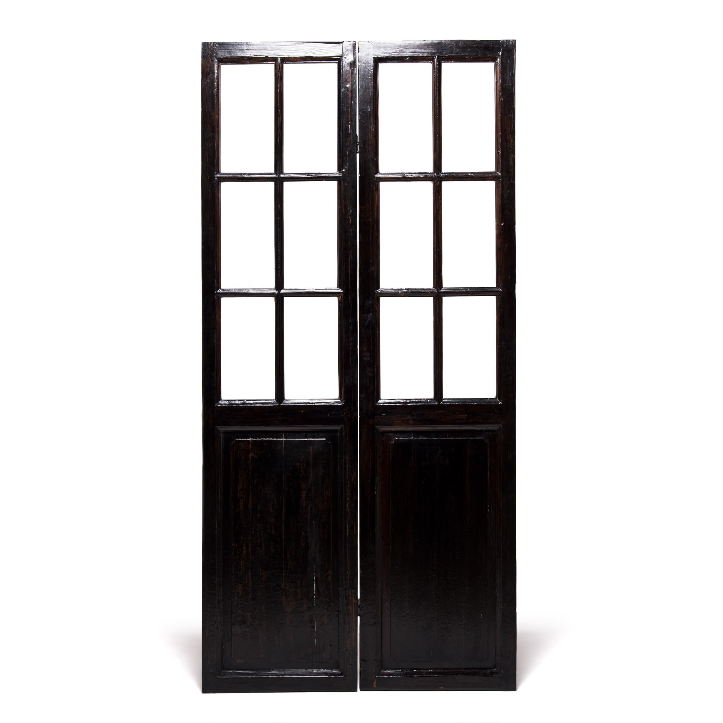 A hallmark of Qing-dynasty domestic architecture, these hand carved doors were originally used in a Provincial courtyard home to allow light and air into a room while maintaining privacy. Paned glass balances the dark-lacquered elmwood frame,
