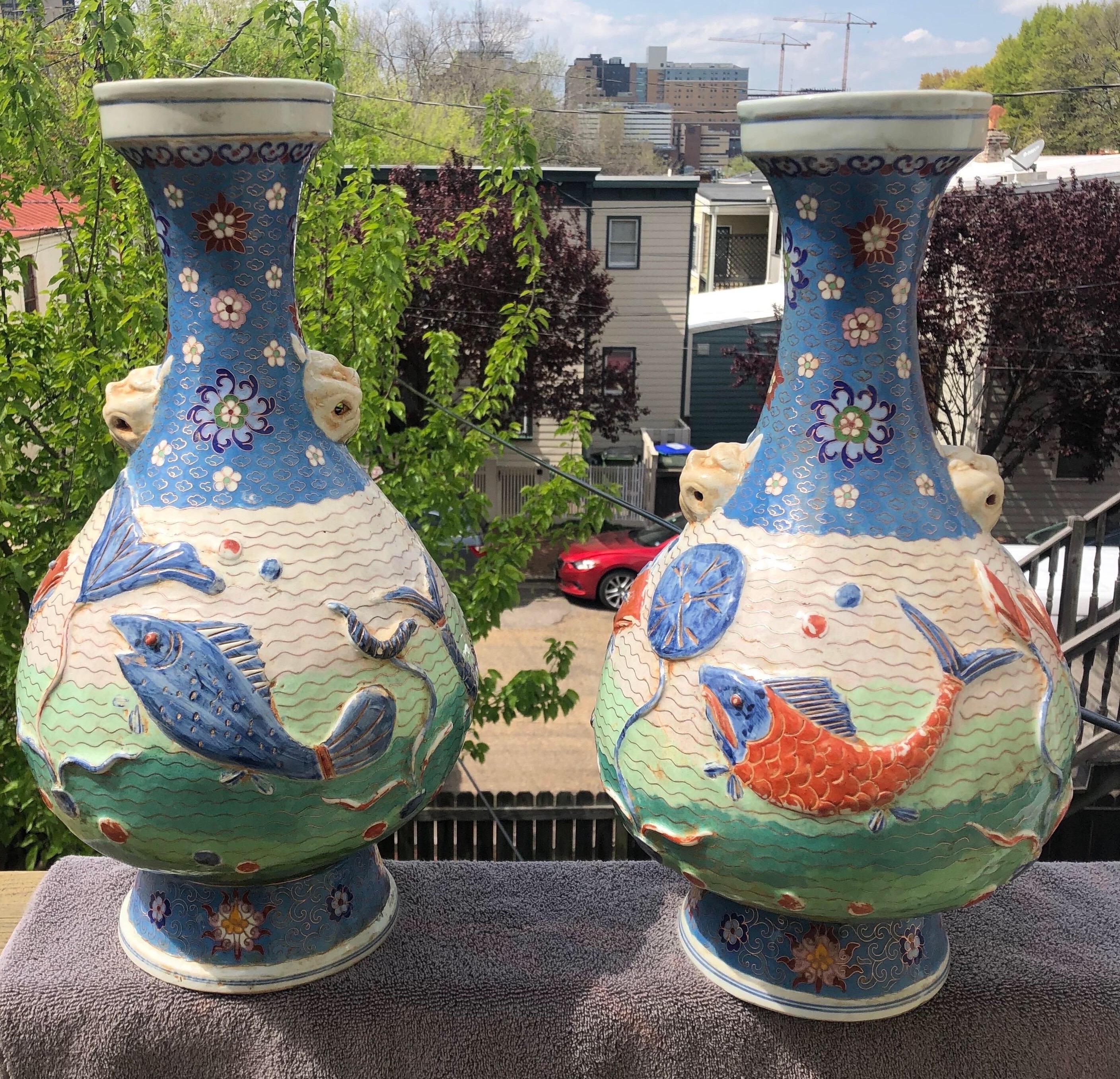 Pair of early 20th century Chinese cloisonne enameled porcelain bottle vases with mask handles, relief molded with fish in a lotus pond on a wire wave ground beneath clouds and flower heads. Vibrant greens, blue and coral colors.
 