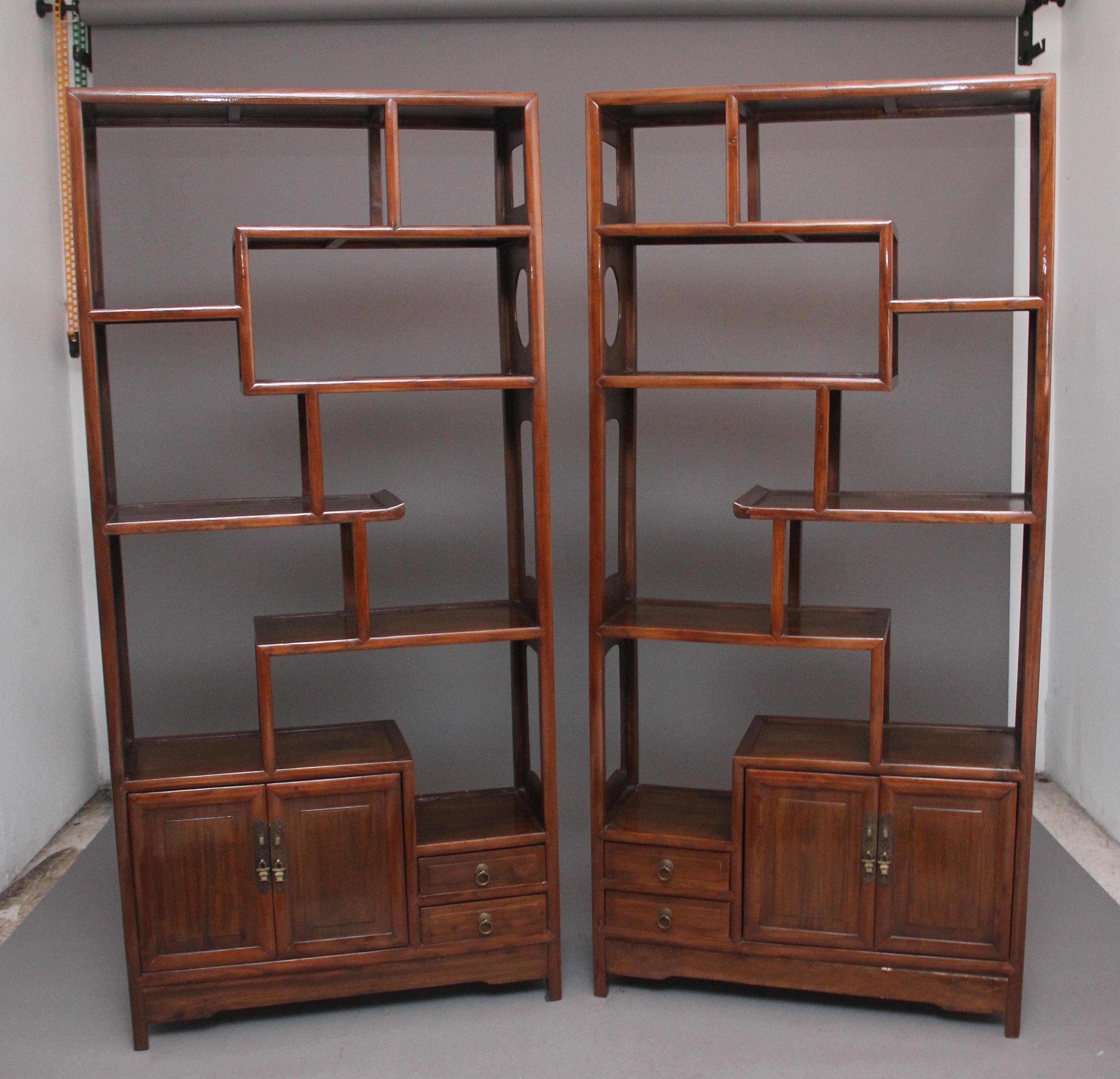 A pair of early 20th Century Chinese hardwood display cabinets, each cabinet having a nice arrangement of shelves with cupboards and drawers below, all having the original brassware, the sides of the cabinets having decorative shaped cut outs. Ideal